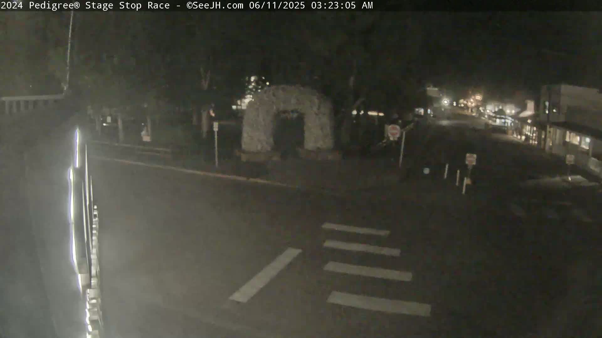 A nighttime street scene shows a roadway with a crosswalk and a stone archway in the background under dark conditions.