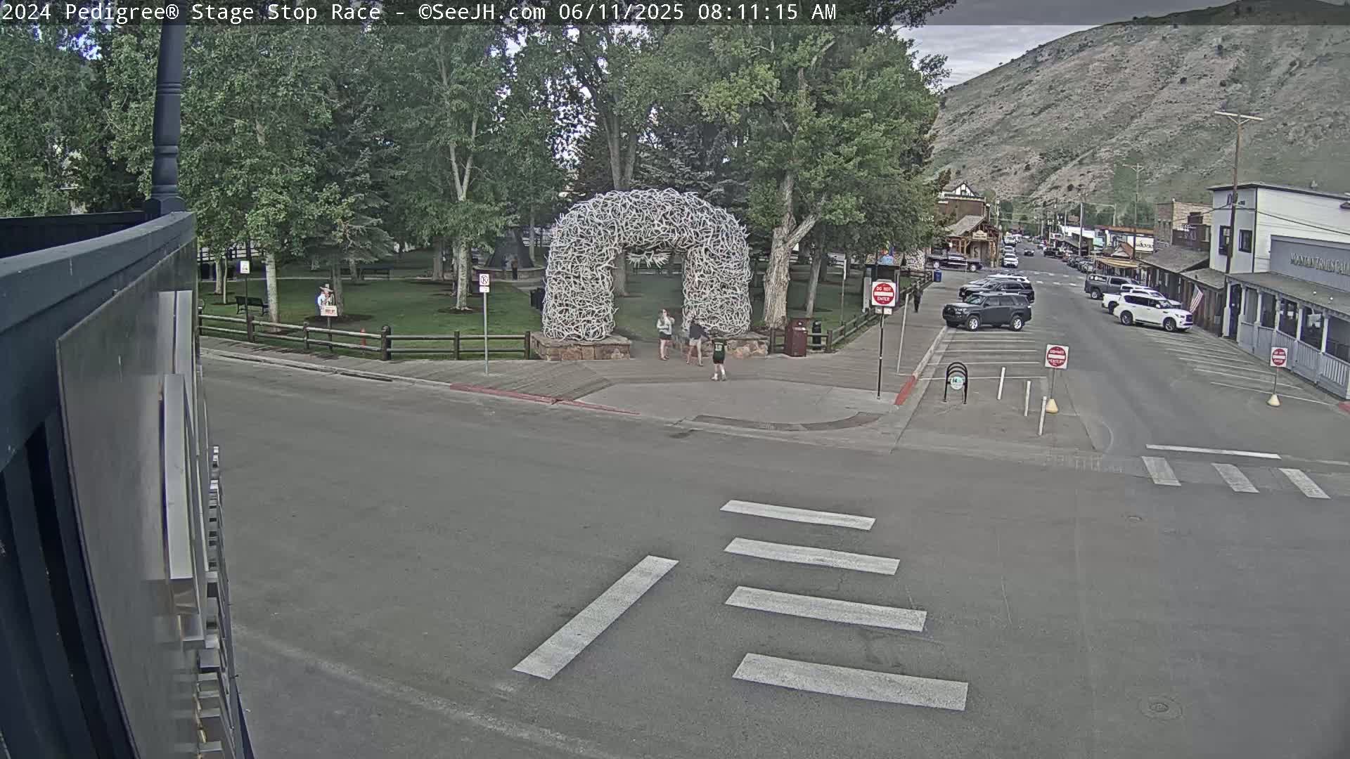 A town square with a large antler archway, a few pedestrians, and parked cars, is visible on an overcast day.