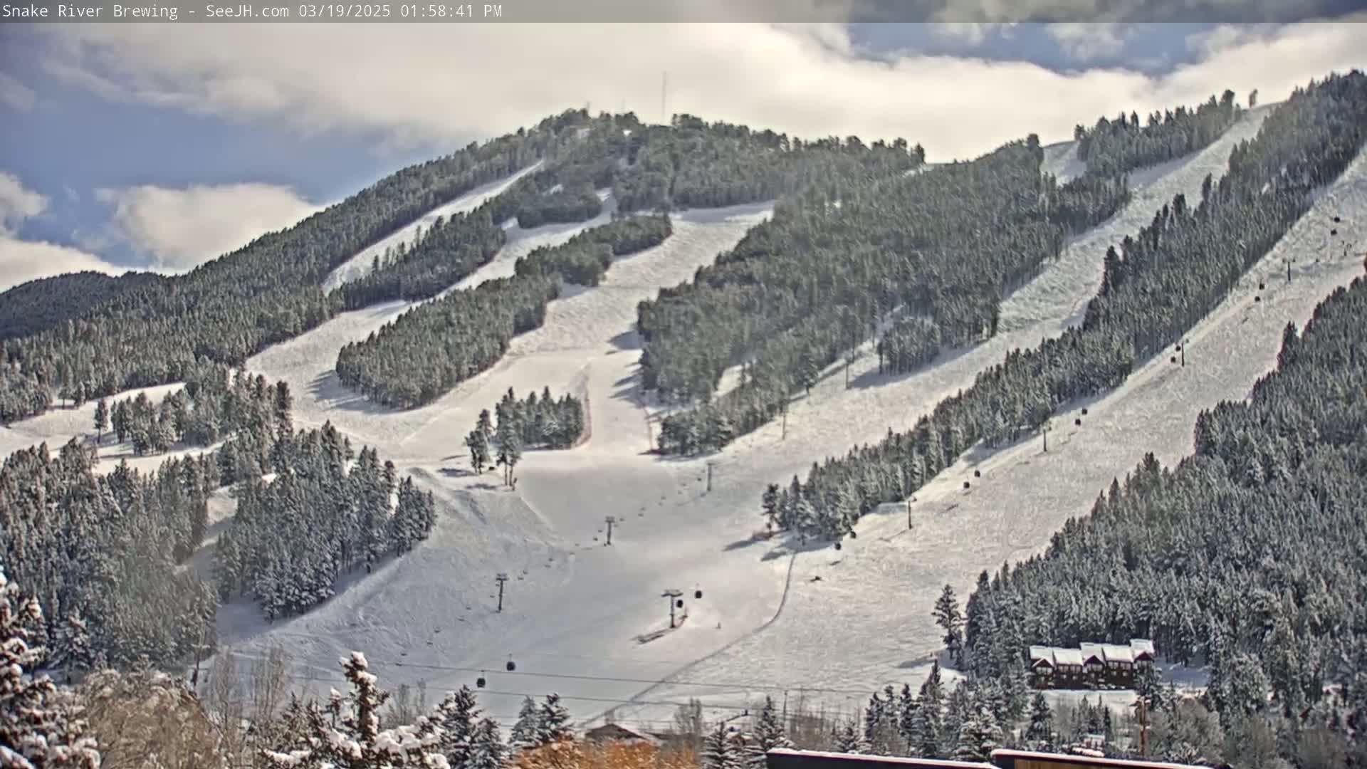 A snow-covered ski resort with numerous ski runs and chairlifts under partly cloudy skies.