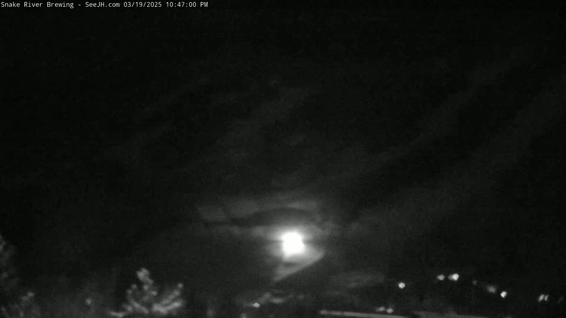 A nighttime scene shows a bright moon partially obscured by clouds above a dark landscape with a few distant lights.