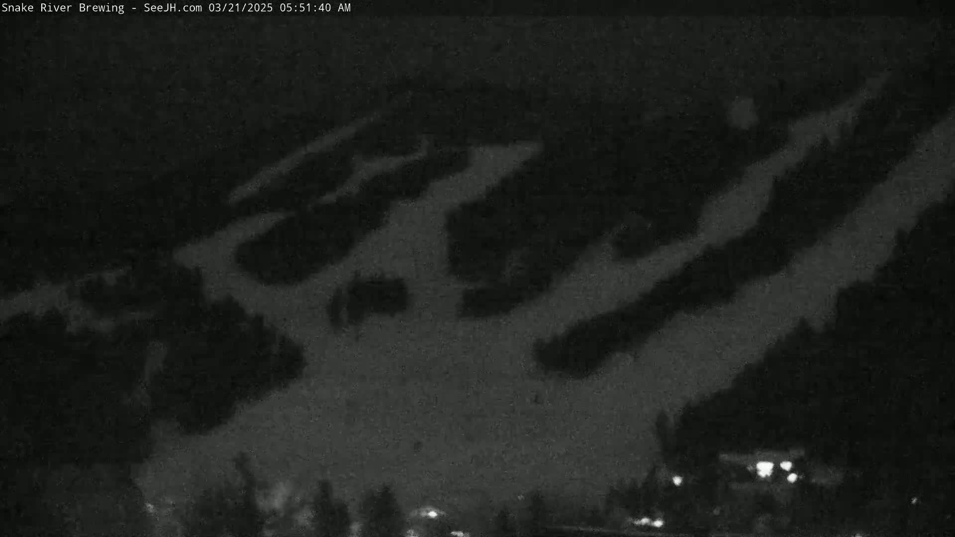 A nighttime, low-light image shows a snow-covered ski slope with faint lights visible at the bottom.