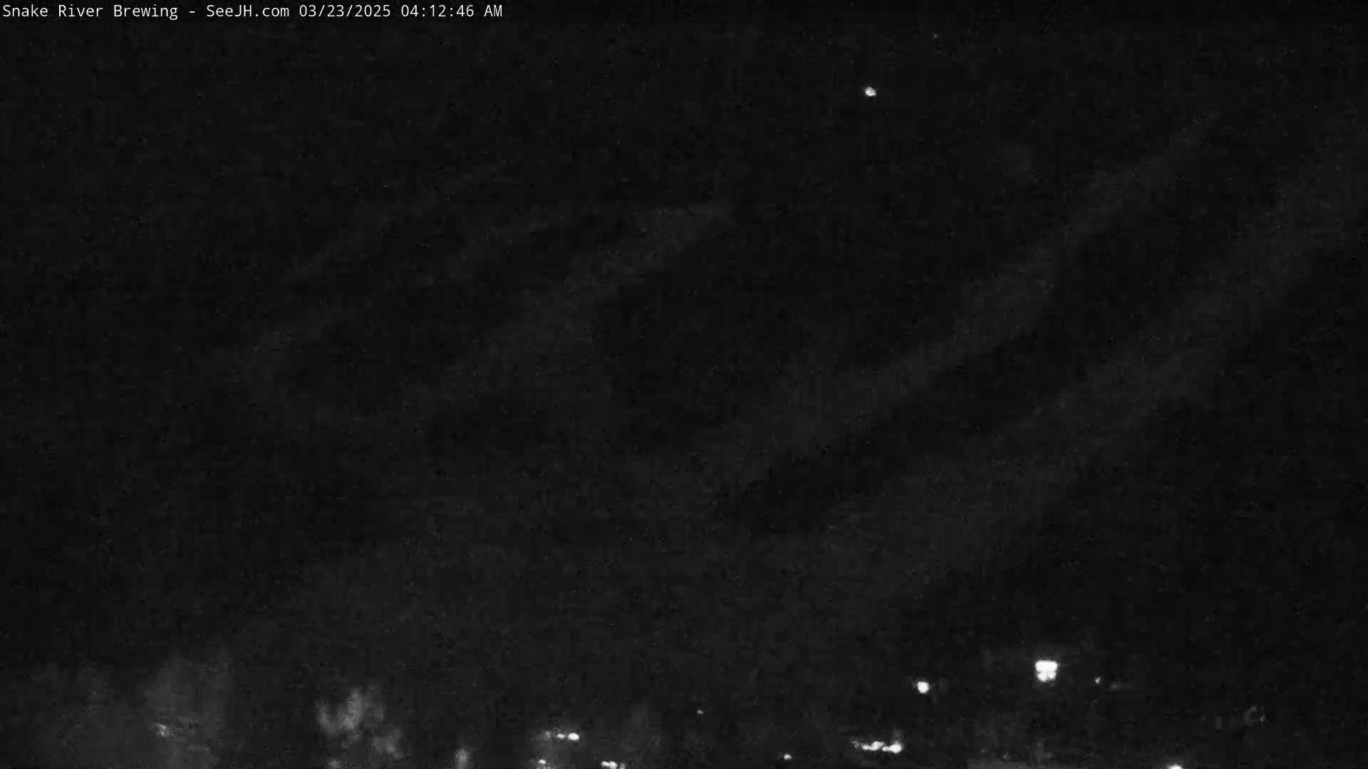 A nighttime view of a dark sky with faint clouds and distant lights on the horizon.