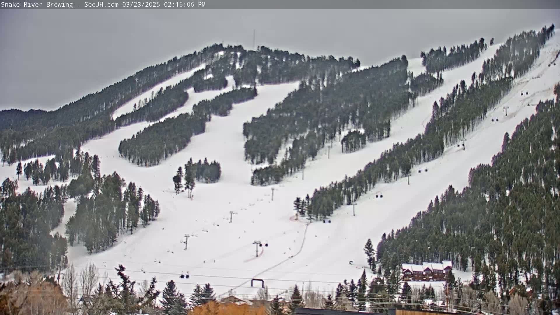 A snow-covered ski slope with several ski lifts and sparsely populated runs is visible under an overcast sky.
