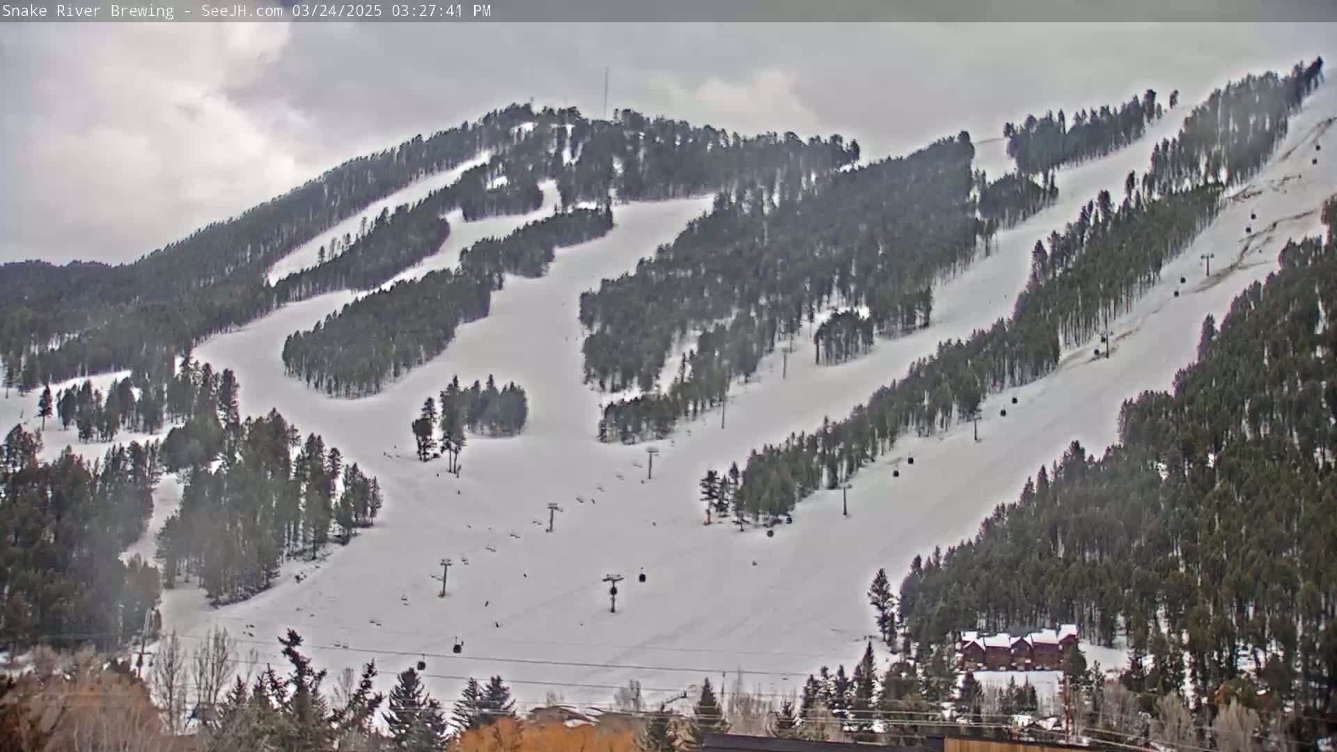 A snow-covered ski resort with numerous ski runs and chairlifts is visible under a cloudy sky.