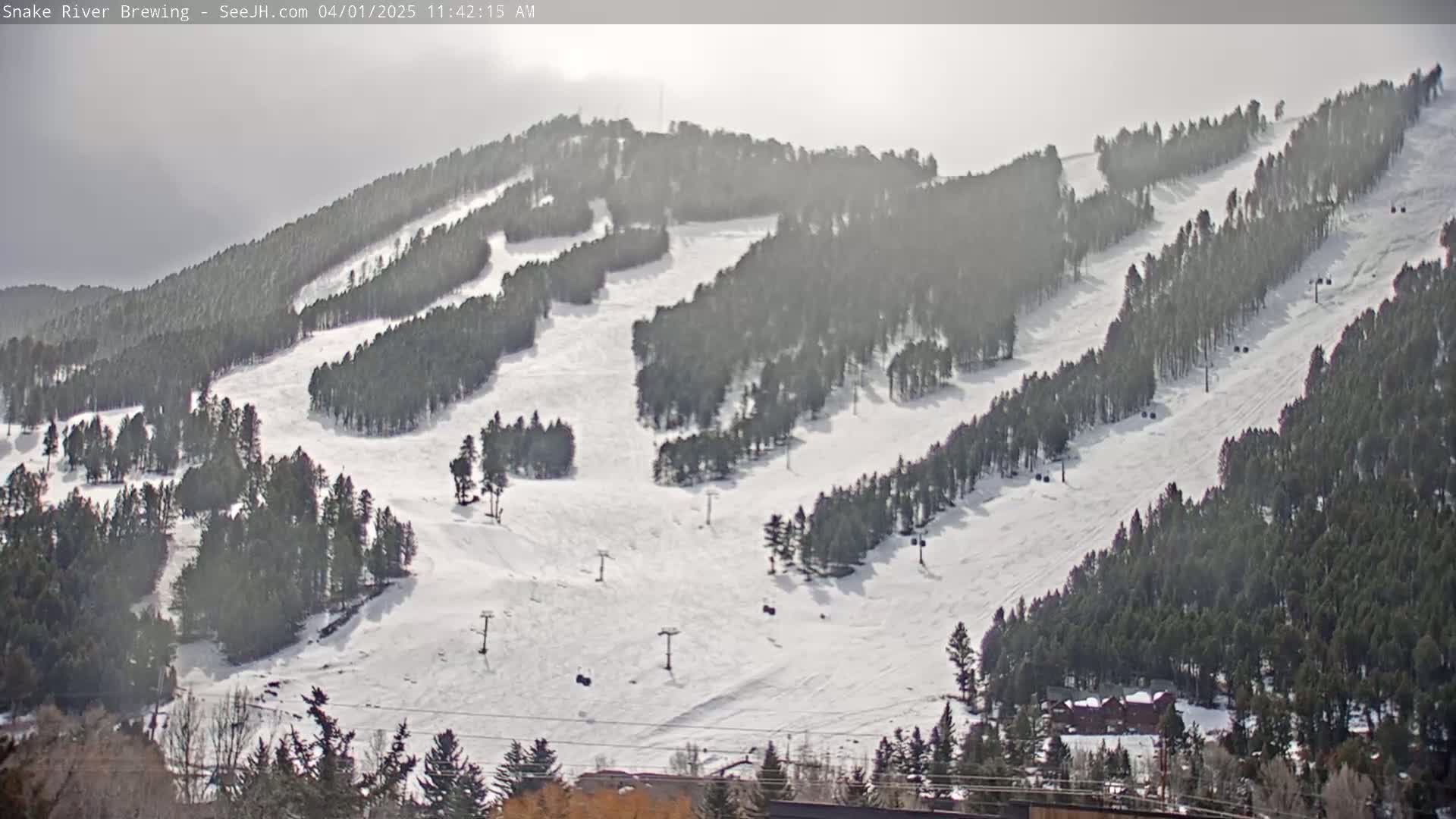 A snow-covered ski resort with numerous runs and ski lifts is visible under a hazy, bright sky.