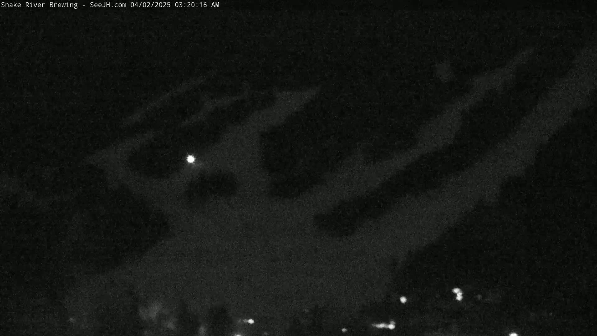 A nighttime view of a cloudy sky with a bright light visible, and a few faint lights on the horizon.
