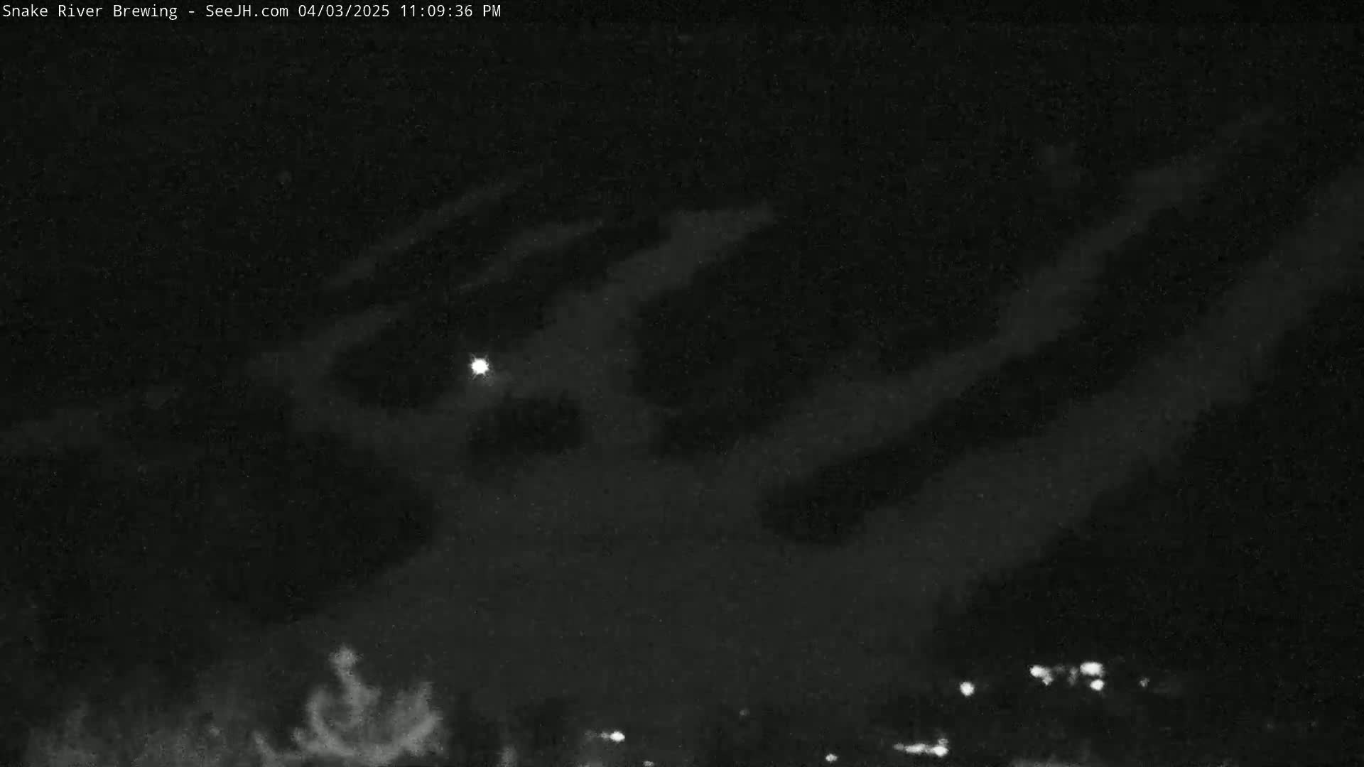 A nighttime, cloudy sky shows a bright light and distant, faint lights on the ground.