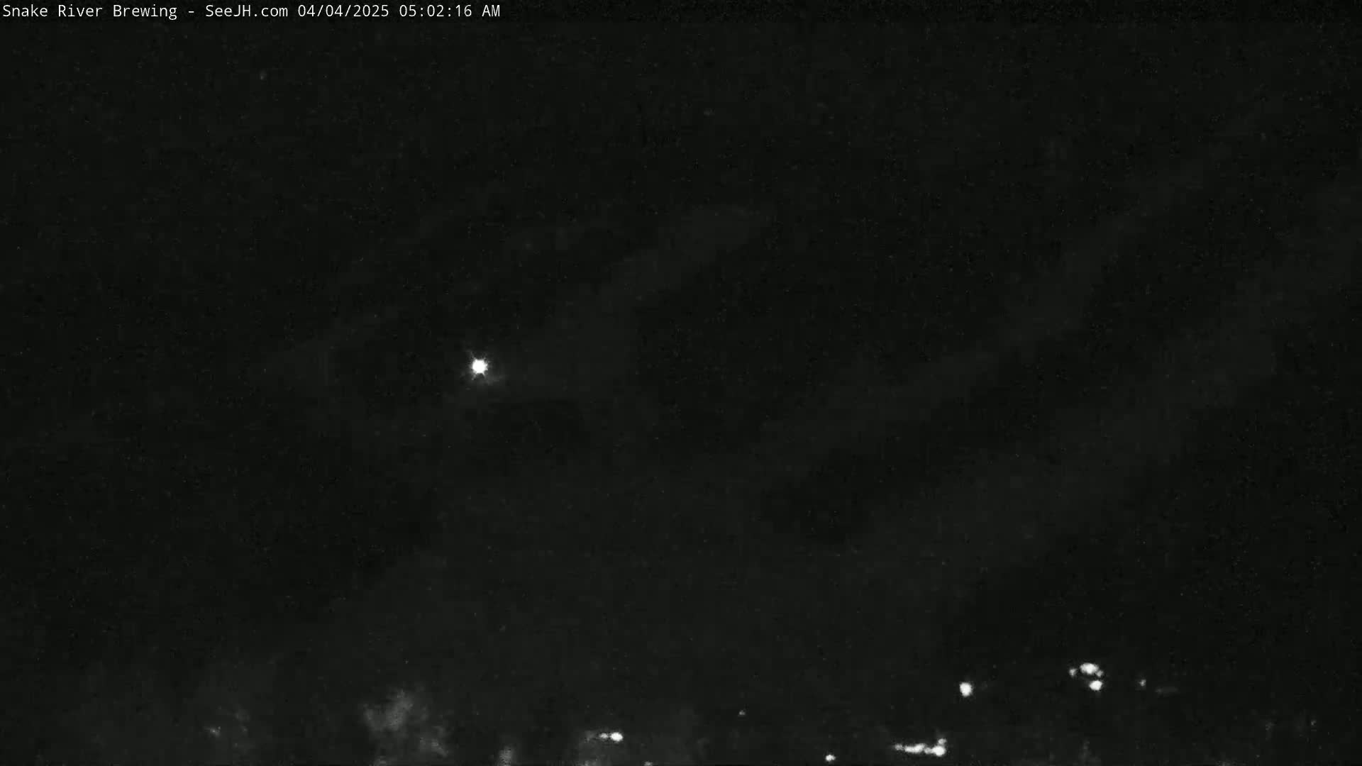 A bright light is visible in a dark night sky with faint clouds and a few distant lights on the ground.