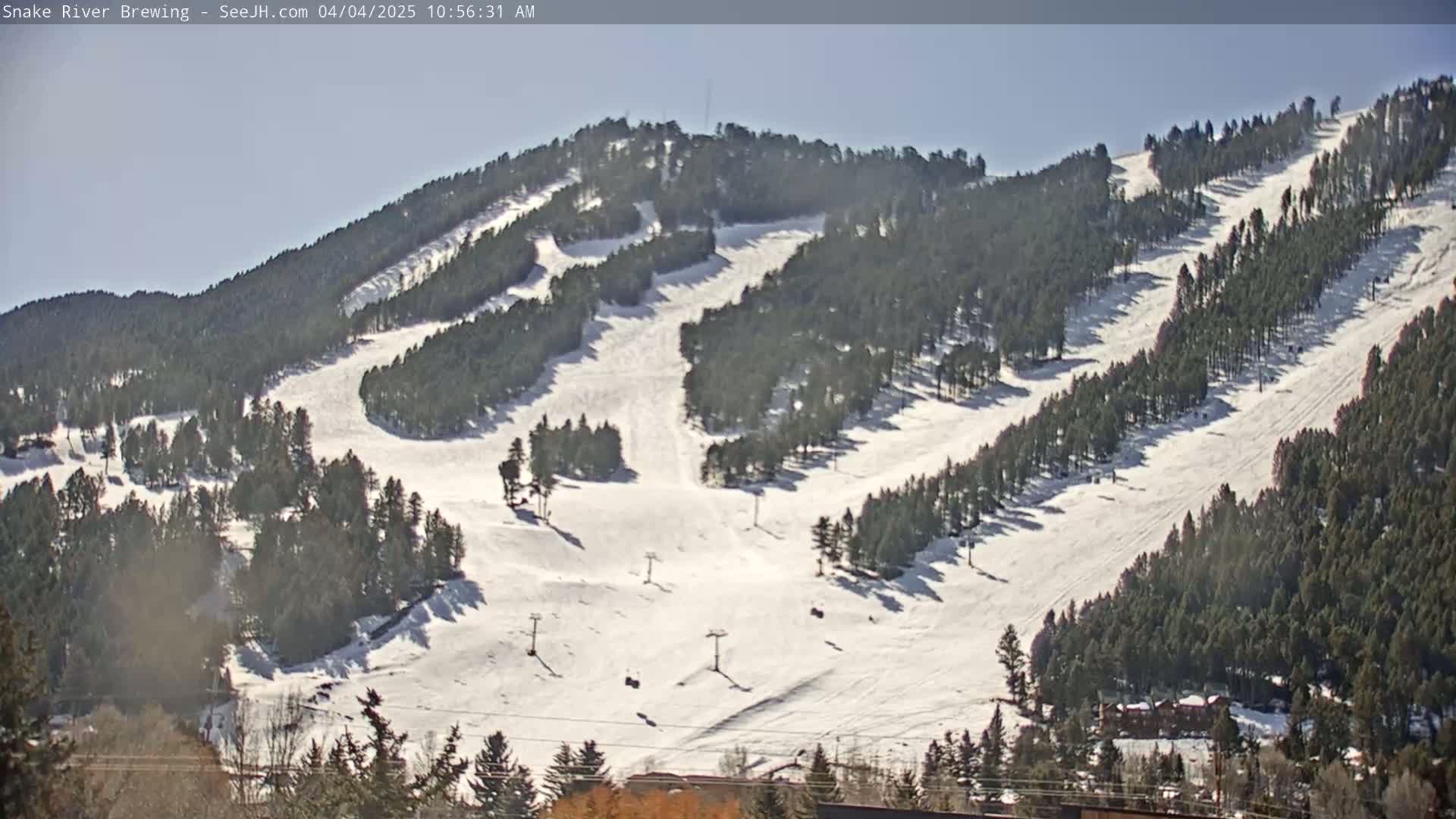 A snow-covered ski slope with several ski lifts and evergreen trees is visible under a sunny sky.