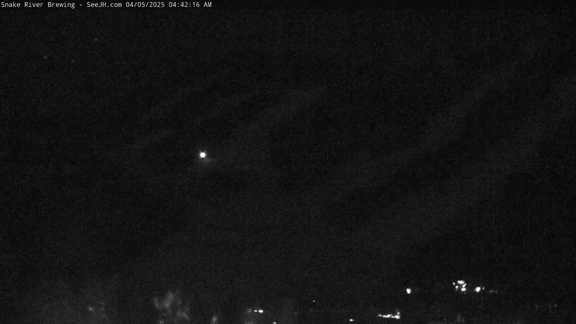 A nighttime, low-light image shows a mostly clear sky with a bright light source in the distance and faint lights near the horizon.