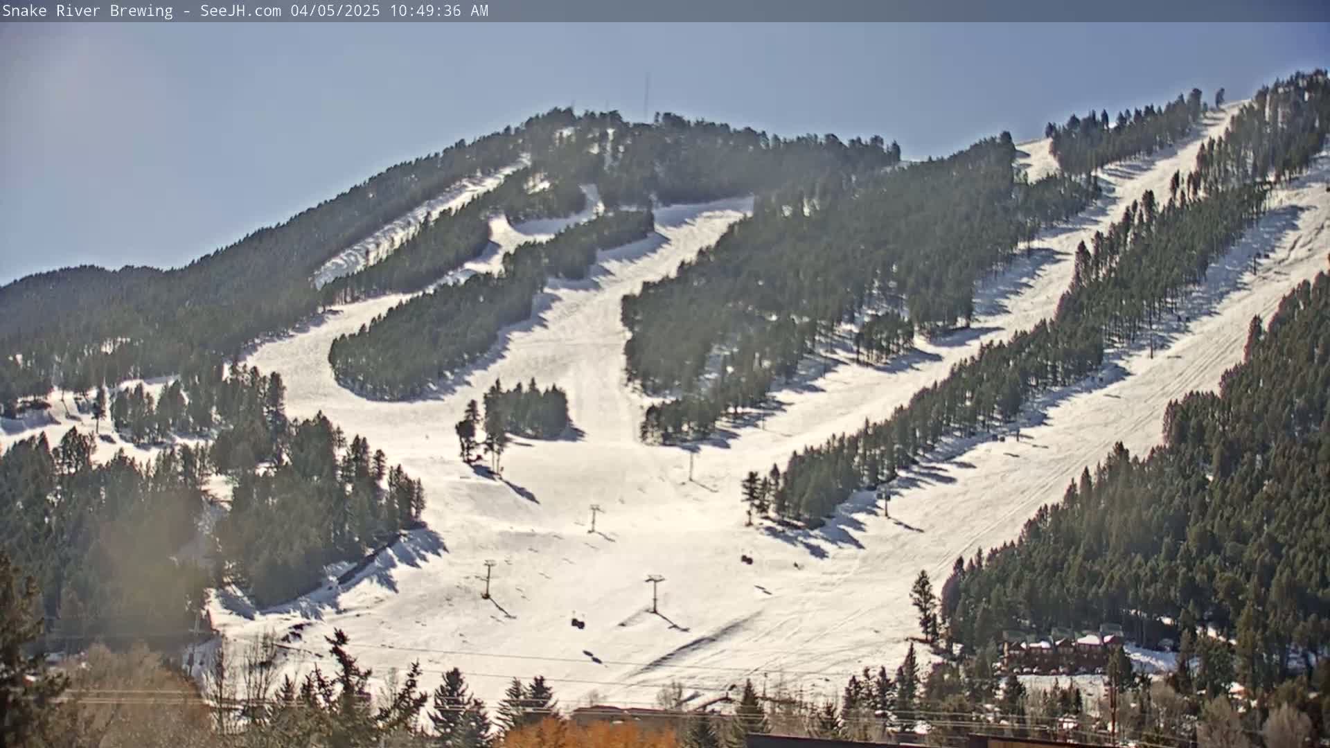 A snow-covered ski slope with several ski lifts is visible on a sunny day, nestled amongst evergreen trees.