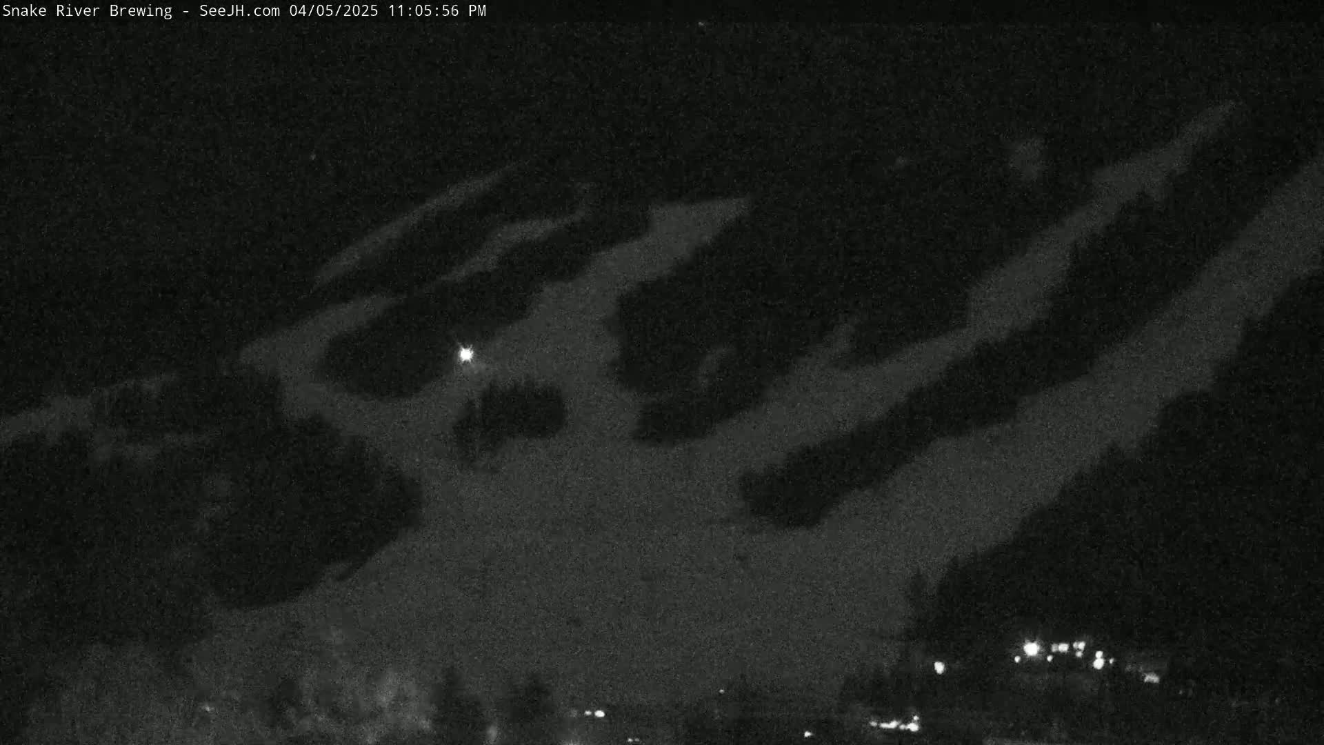 A nighttime, low-light image shows a snow-covered hillside with faint lights visible in the distance.