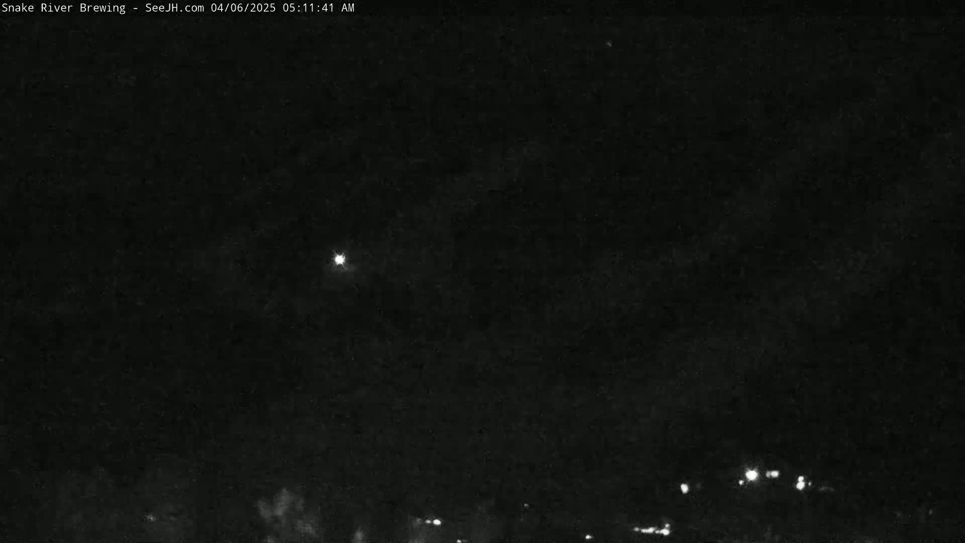 A nighttime image shows a mostly clear sky with a bright light source and faint lights on the horizon.