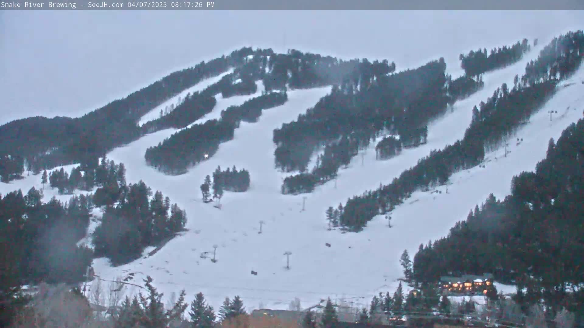 A snow-covered ski slope with several ski lifts and dark evergreen trees under an overcast sky.