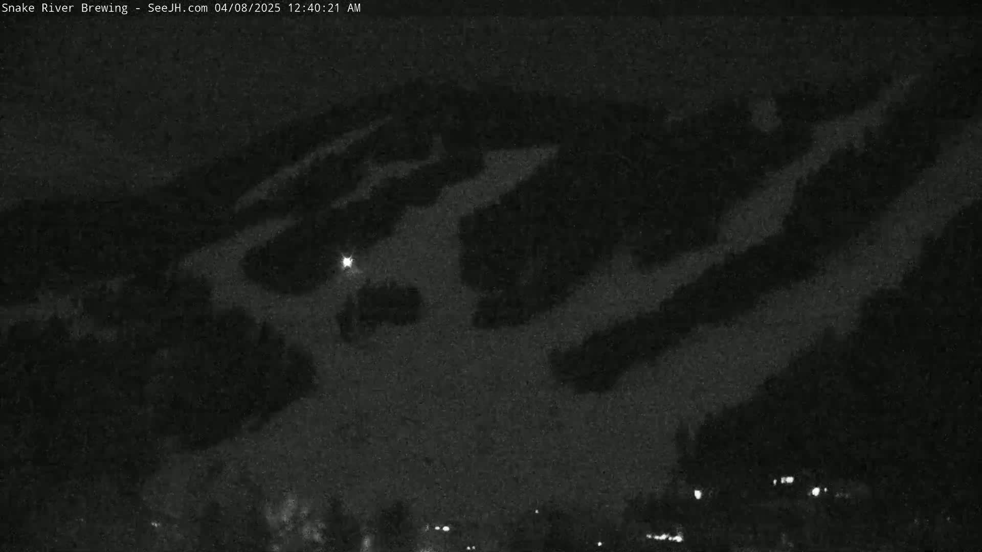 A nighttime, low-light image shows a snow-covered hillside with a few faint lights visible in the lower right corner.
