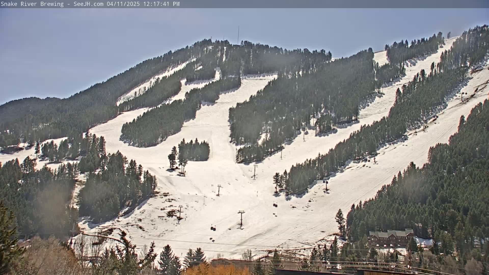 A snow-covered ski resort with numerous runs and ski lifts is visible under a clear, sunny sky.
