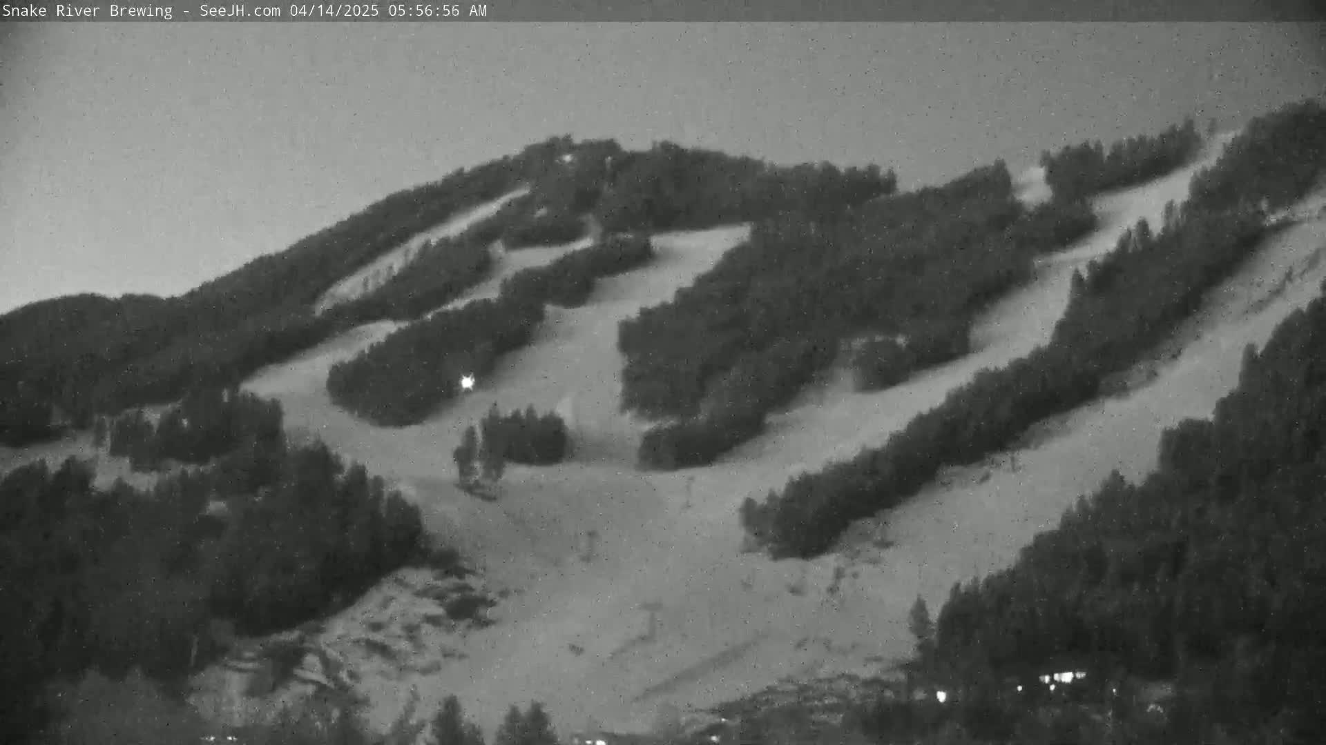 A snow-covered hillside with sparsely wooded areas and ski runs is visible under a dark, possibly nighttime sky.