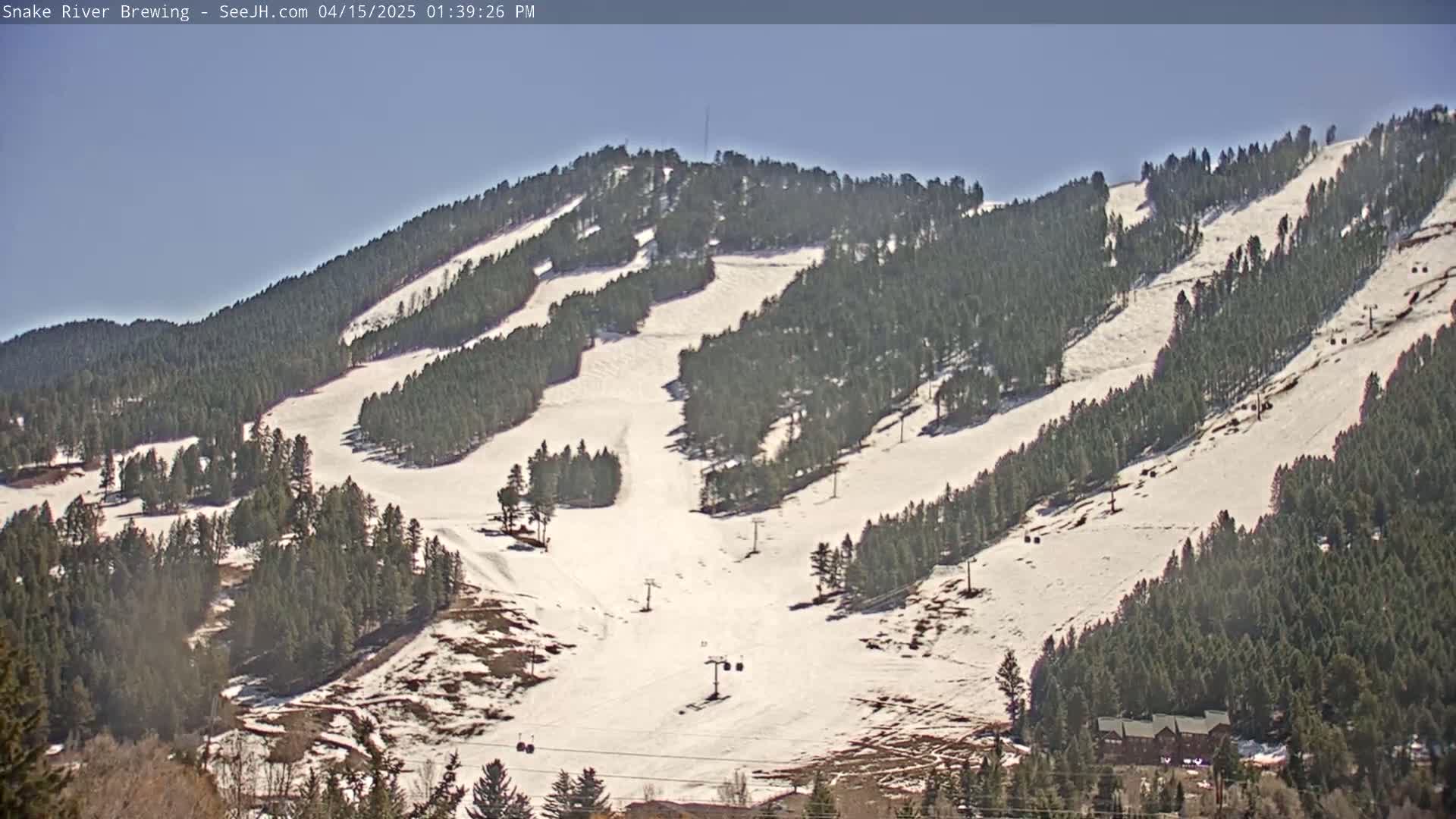 A snow-covered ski slope with several ski lifts is visible on a clear, sunny day, surrounded by evergreen trees.