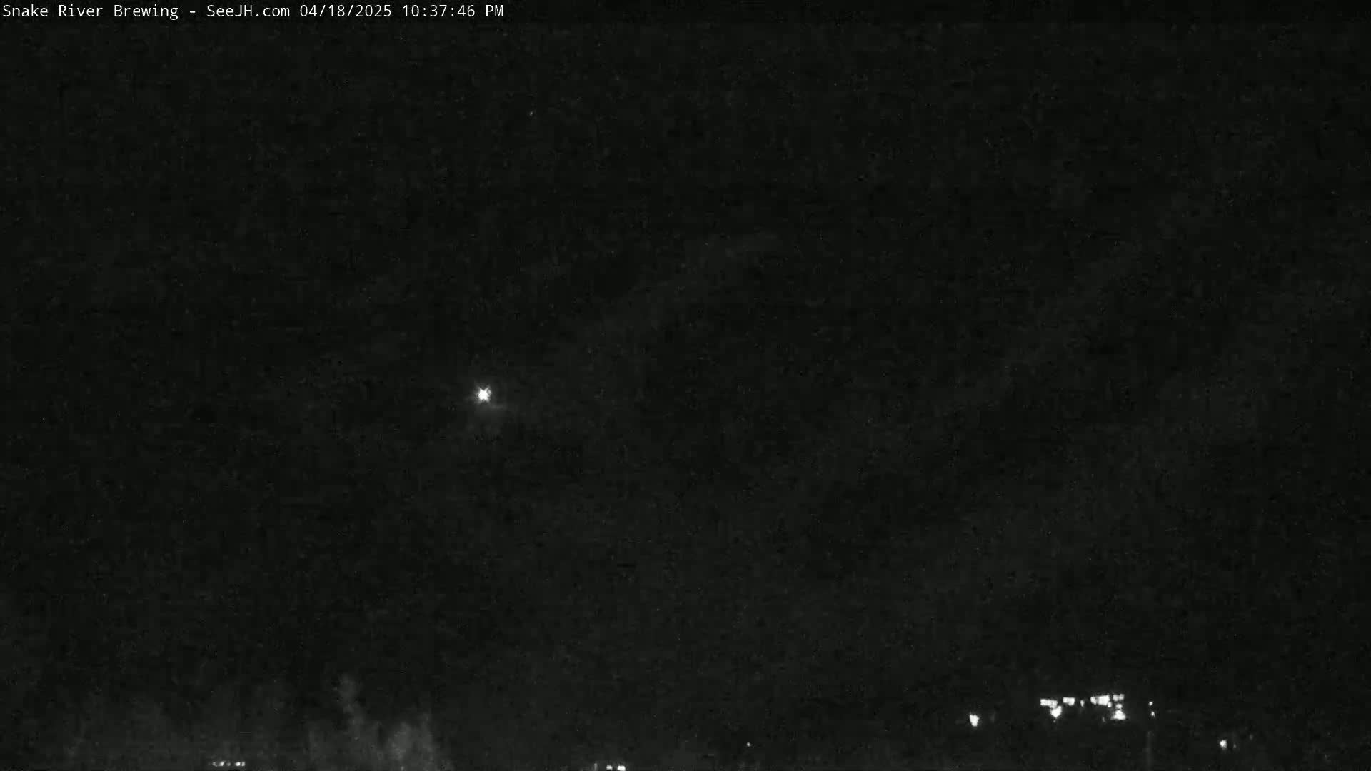 A bright light is visible in a dark night sky above a dimly lit landscape.