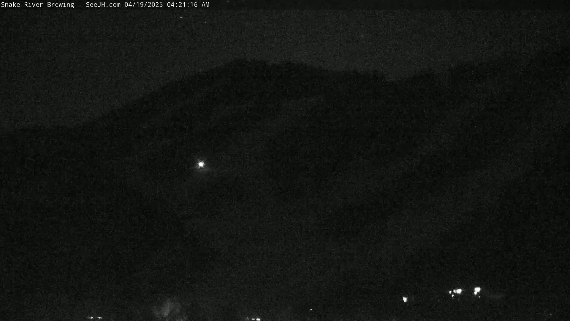 A nighttime long shot shows a dark mountain silhouetted against a dark sky with a single bright light in the mid-ground.