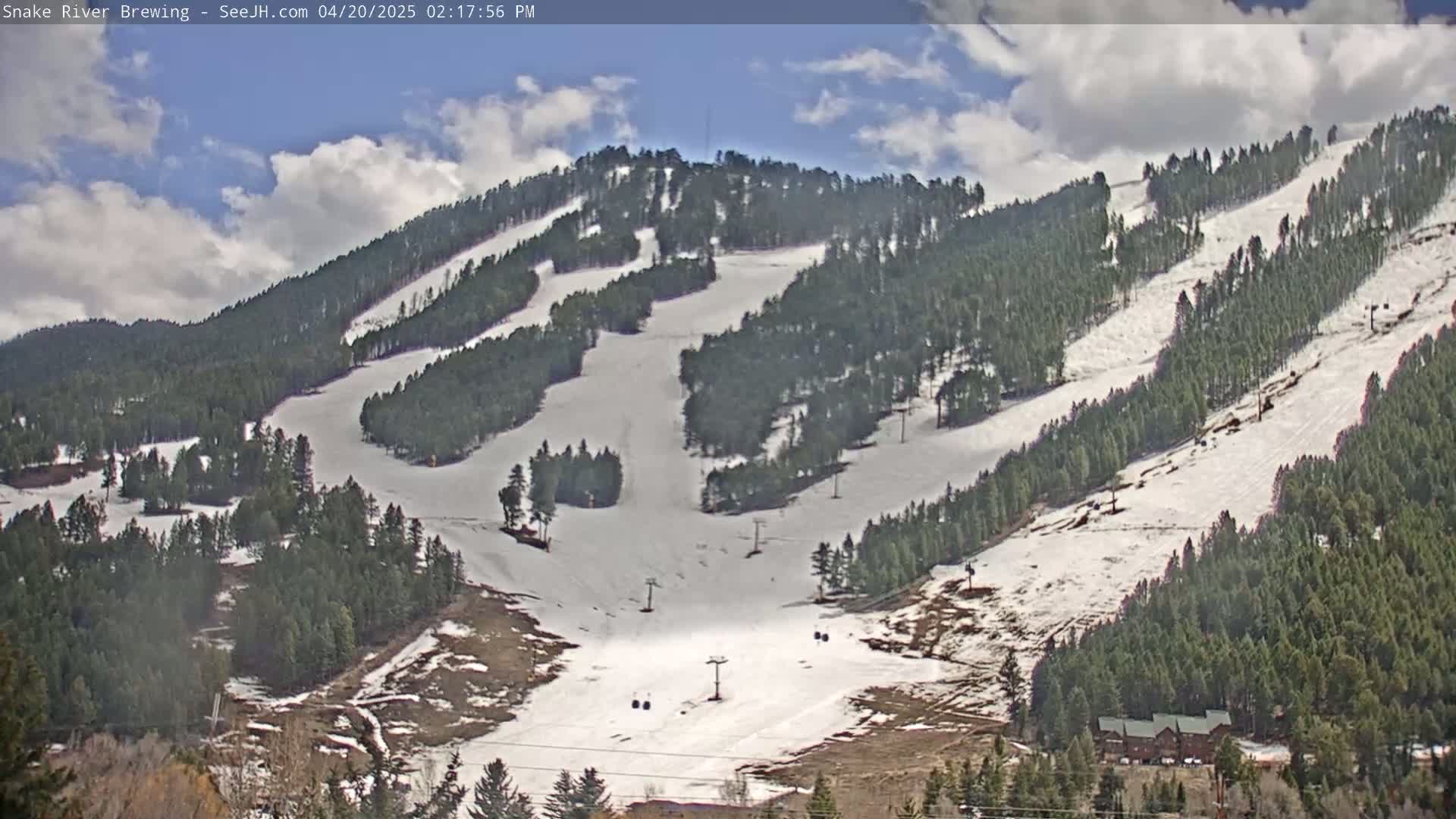 A snow-covered ski slope with several ski lifts and evergreen trees is visible under partly cloudy skies.