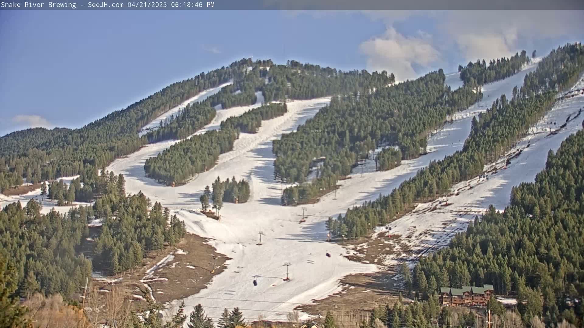 A snow-covered ski resort with several runs and ski lifts is nestled among evergreen trees under a partly cloudy sky.