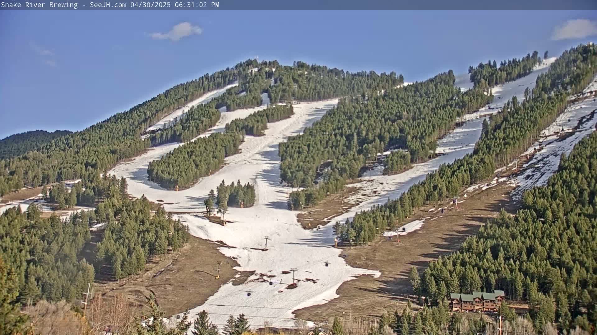 A sunny, snow-covered ski slope on a mountainside, surrounded by evergreen trees.