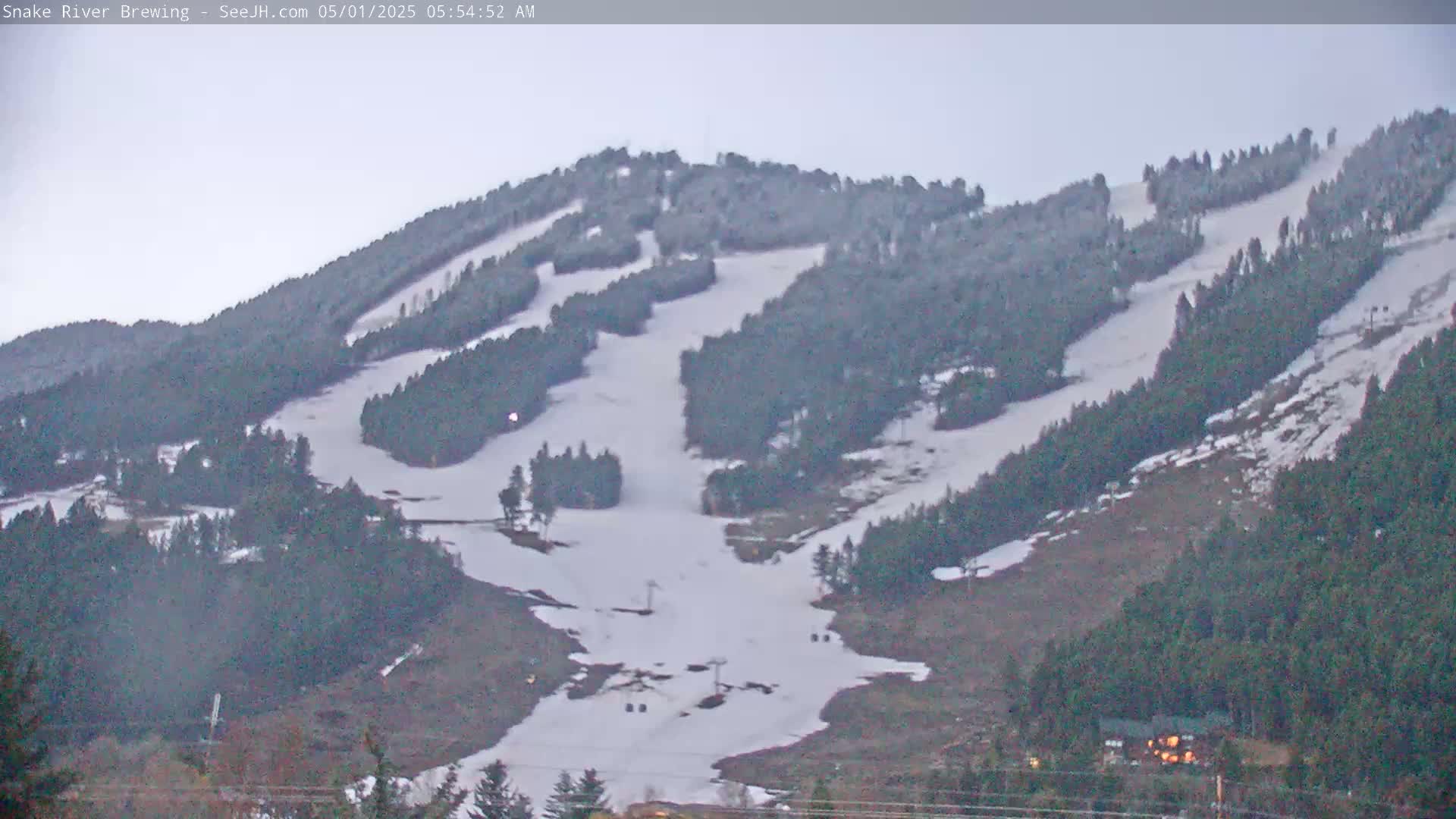 A snow-covered ski slope on a cloudy day is nestled among dark evergreen trees.
