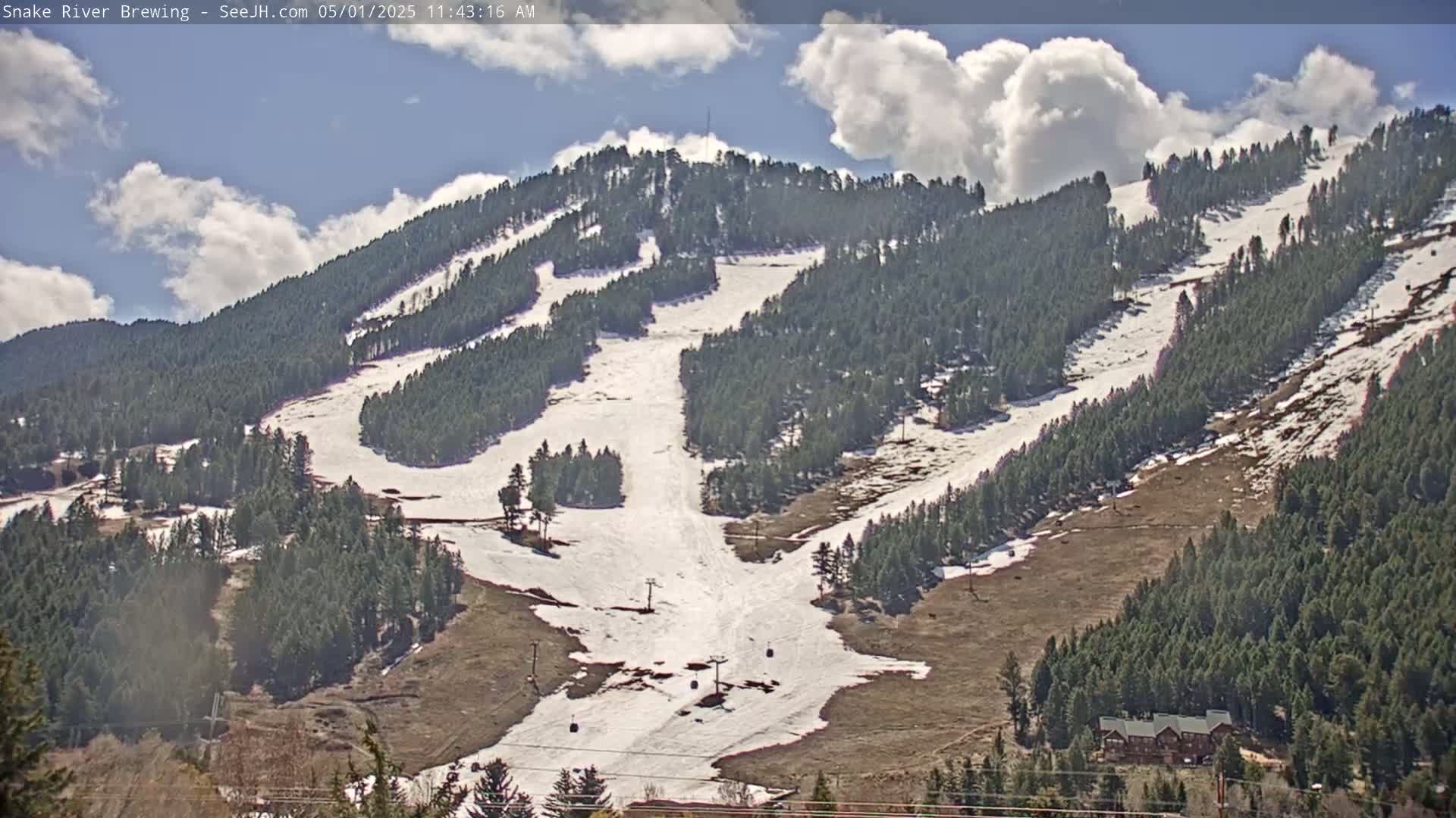 A partly cloudy day reveals a snow-dusted mountainside with ski runs and evergreen trees.
