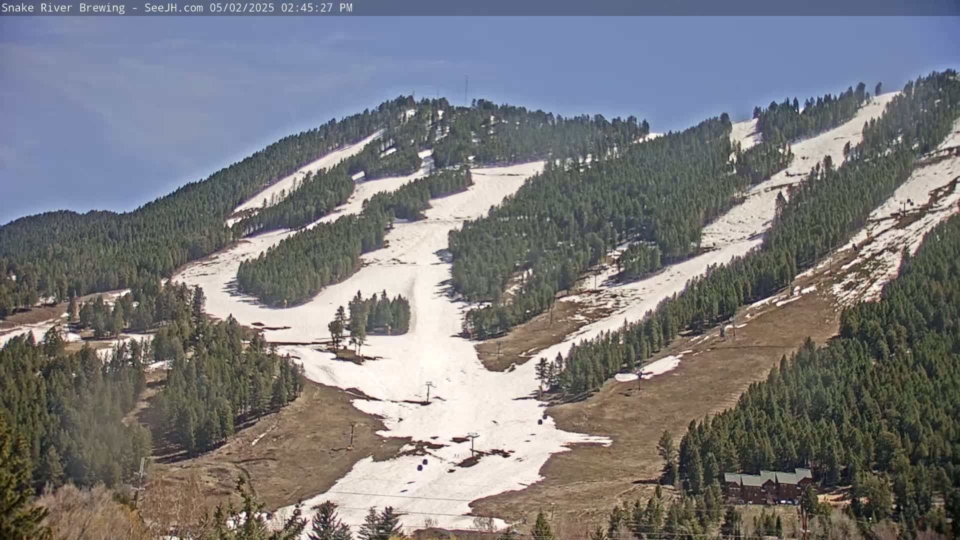 A mostly sunny day reveals a snow-dusted ski slope nestled among evergreen trees on a mountainside.
