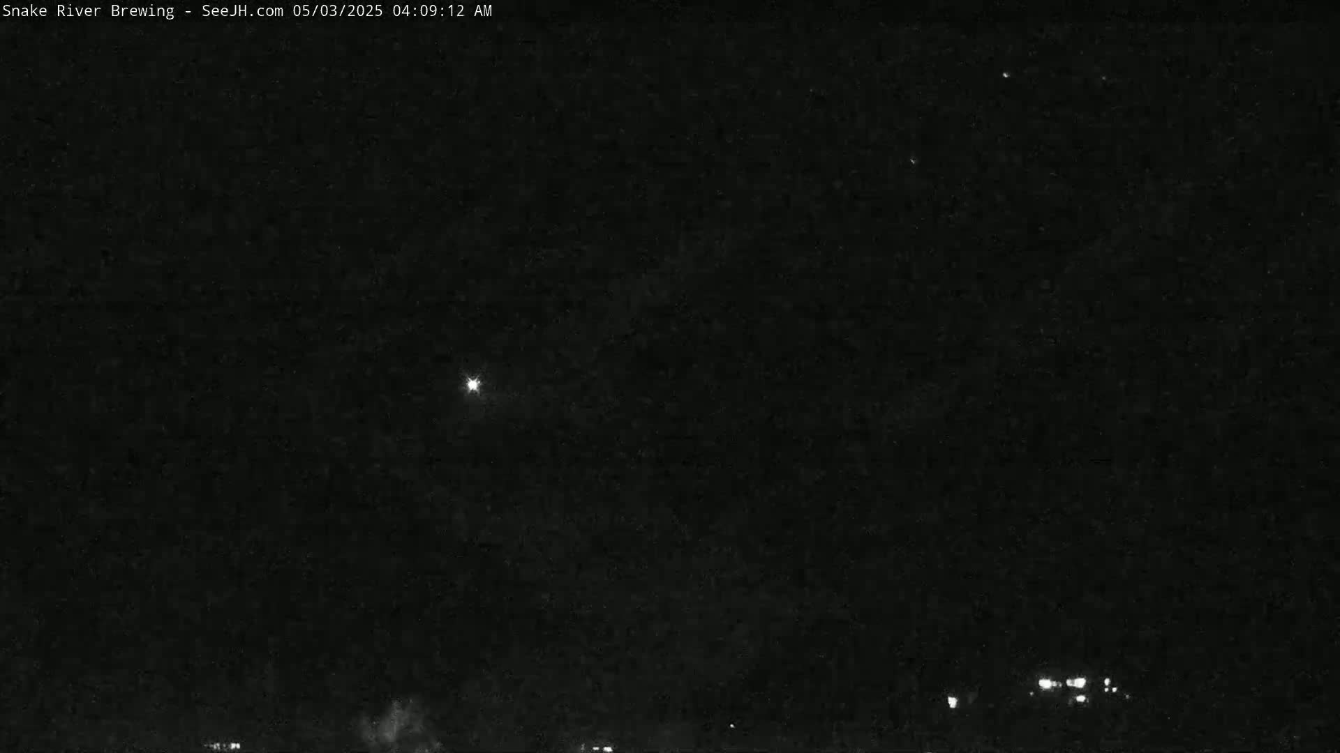 A nighttime, dark sky shows a bright star and faint lights on the horizon.