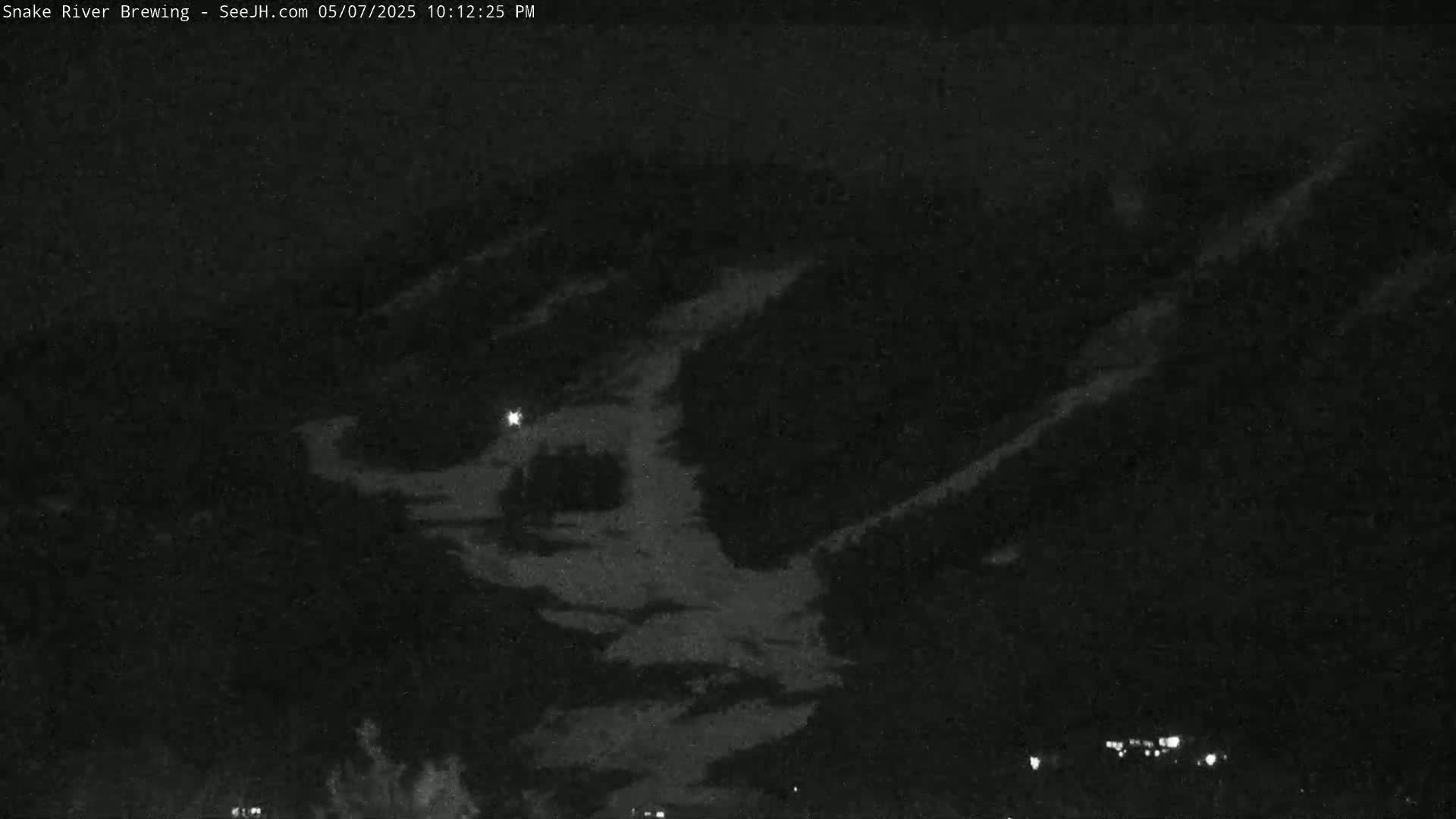 A nighttime, low-light image shows a dark landscape with some clouds or possibly snow-covered hills under a dark sky.