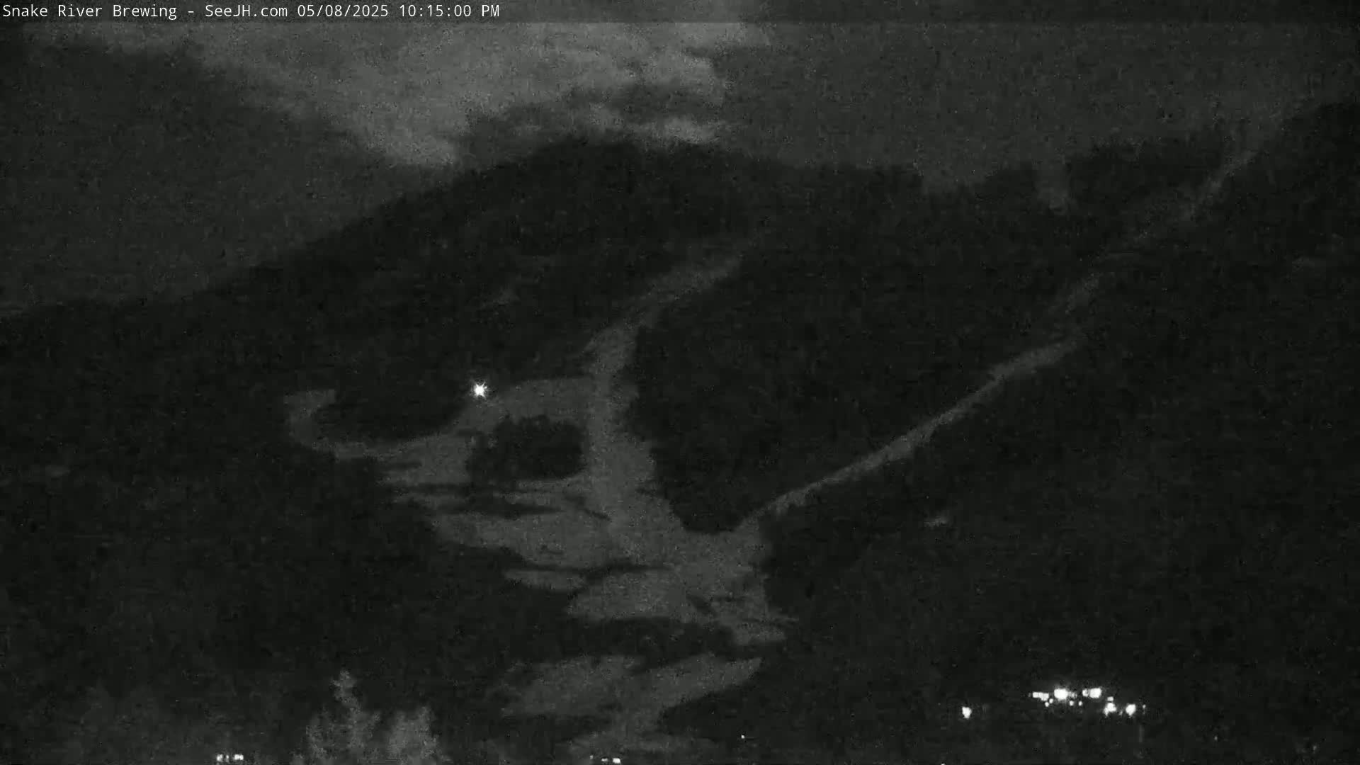 A nighttime view shows a dark mountainside with patches of light-colored snow under a cloudy sky.