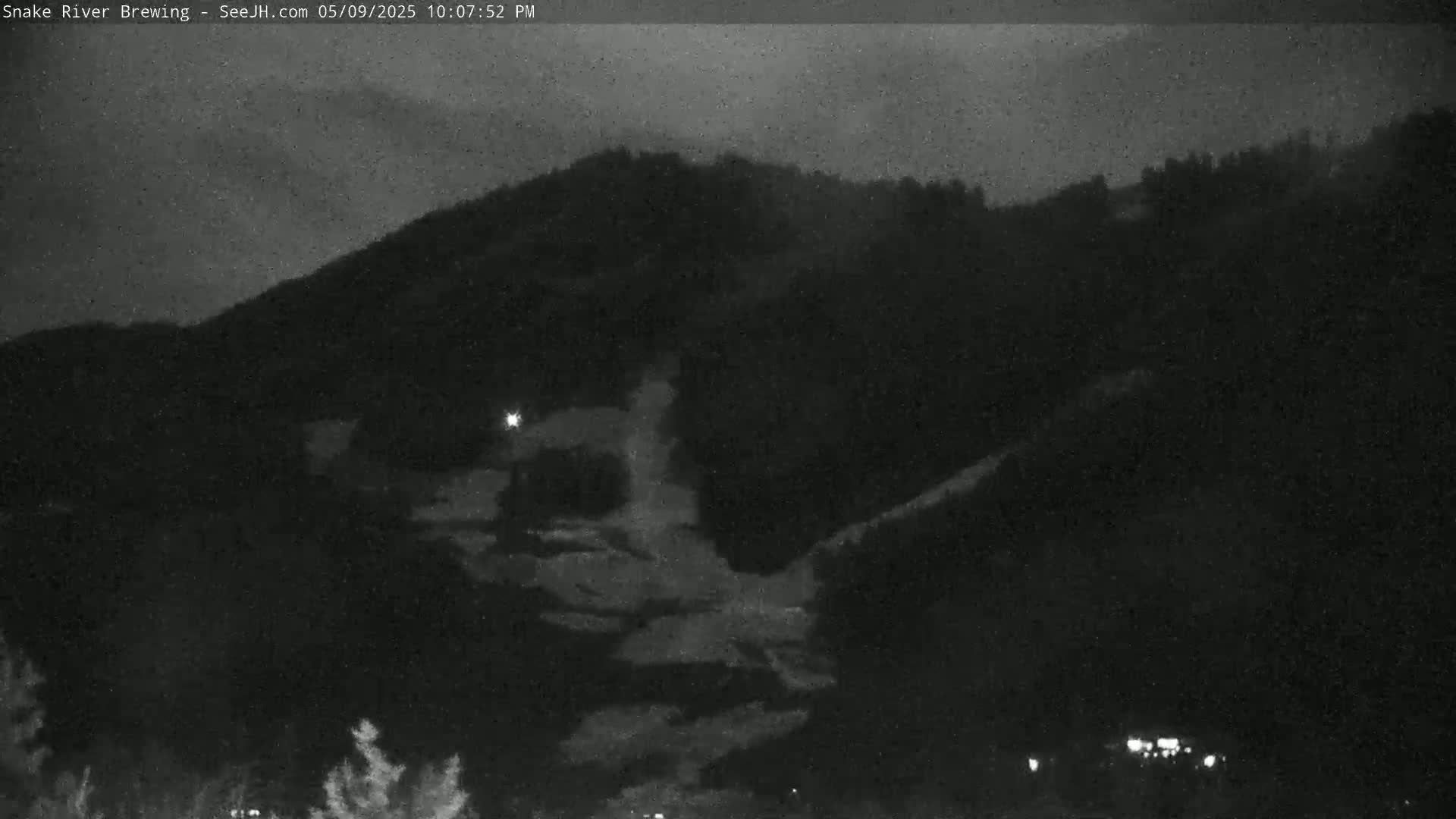 A nighttime, low-light view of a dark, tree-covered hill under a cloudy sky.