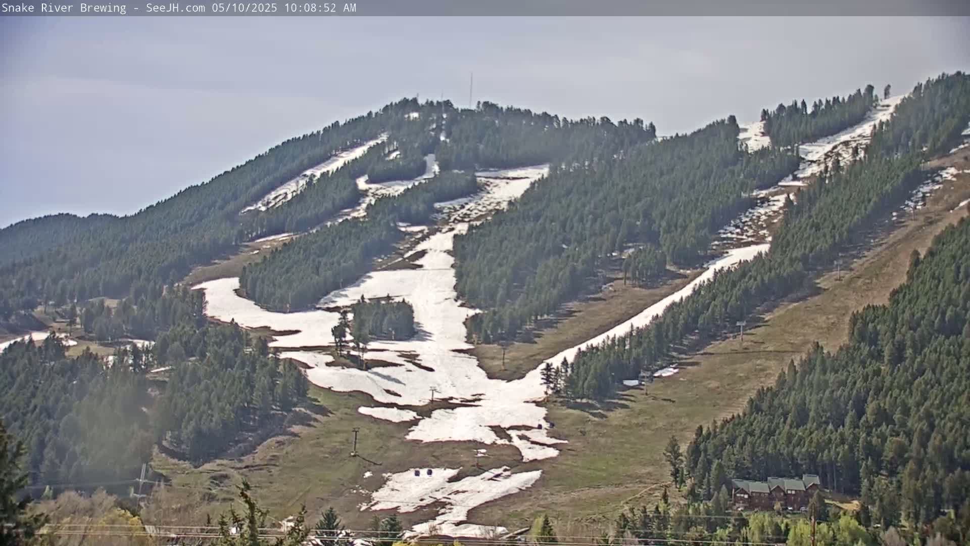 A mountainside ski resort with patchy snow remaining on the slopes, under a clear sky.