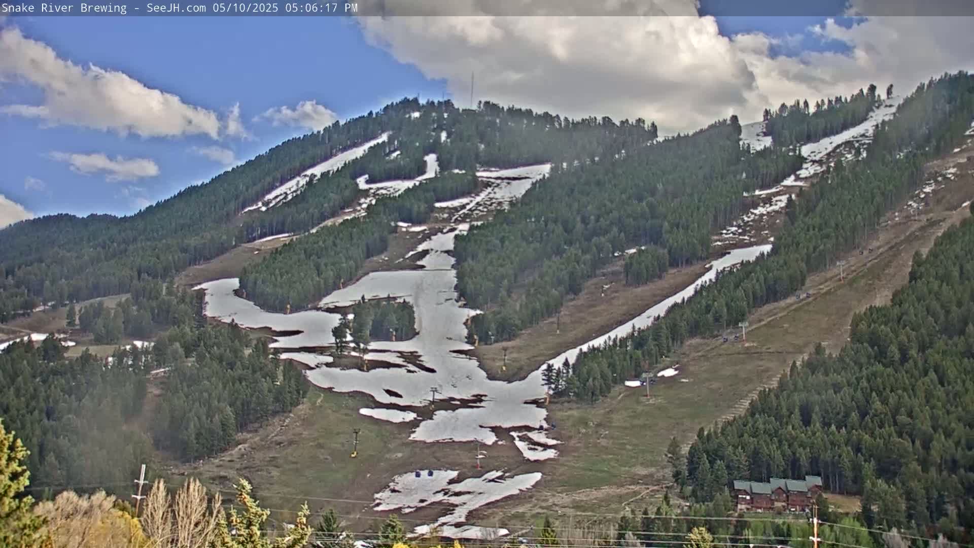 A partially snow-covered mountainside with ski runs, under a partly cloudy sky.