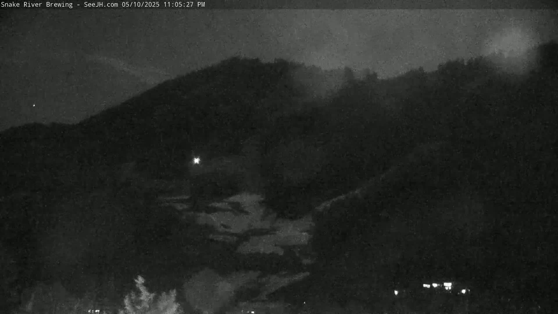 A nighttime, low-light view shows a dark, hilly landscape under a cloudy sky.