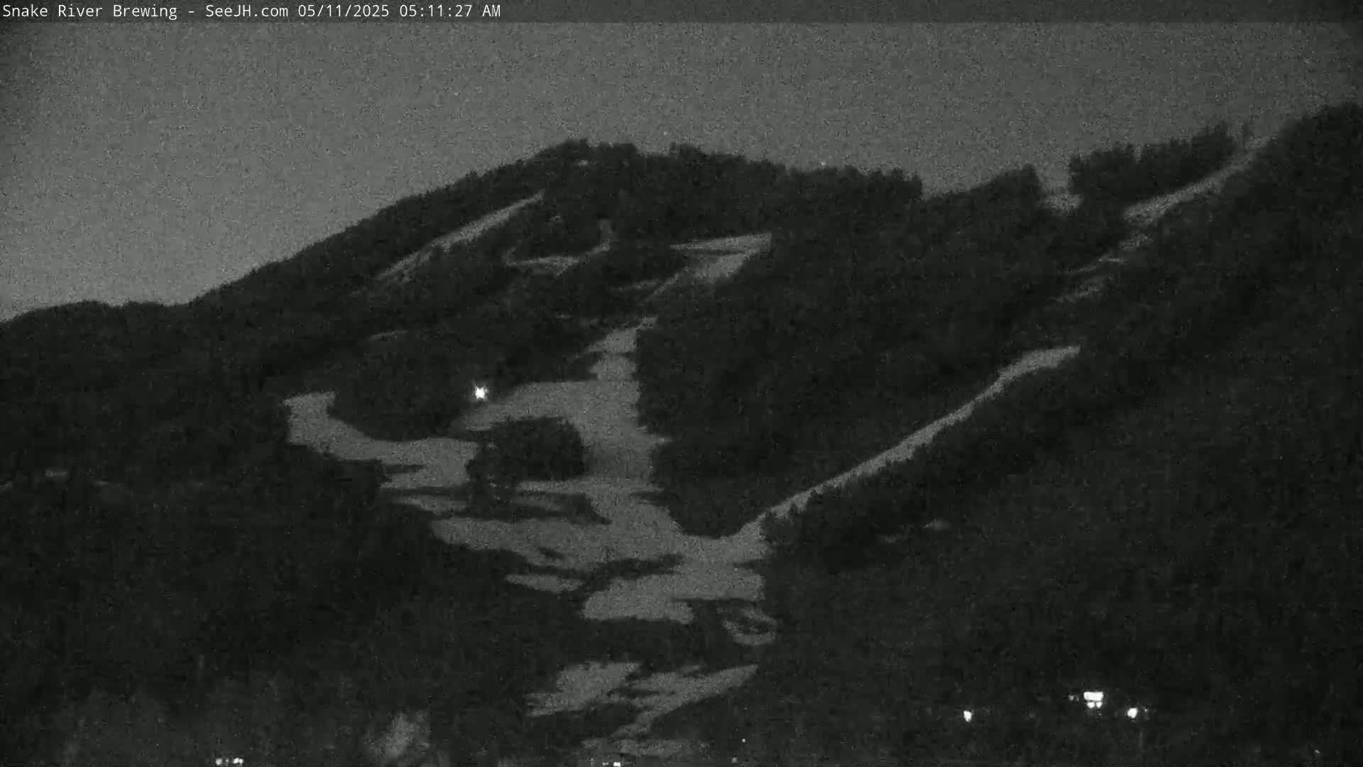 A nighttime, low-light view of a snow-covered hillside with winding paths or ski runs.