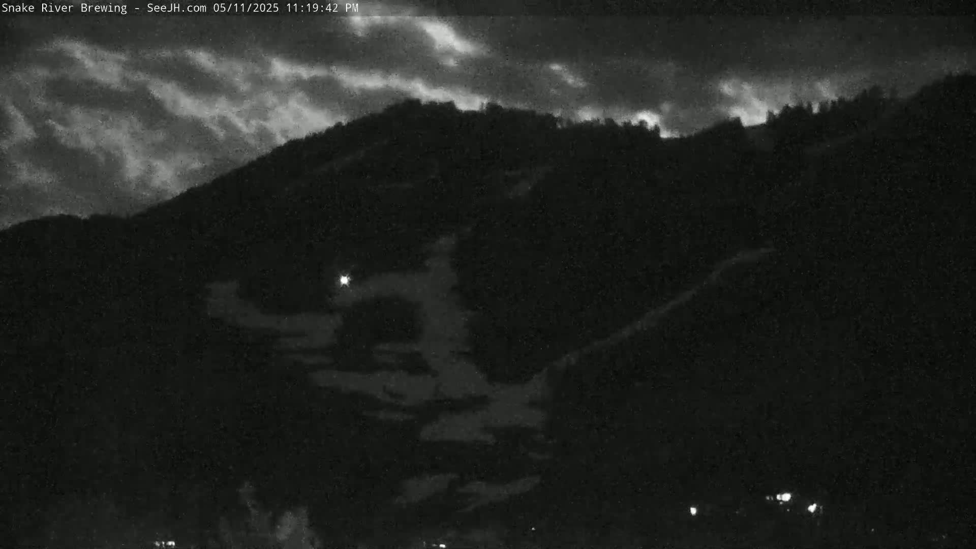 A nighttime view shows a dark mountain silhouetted against a cloudy sky.