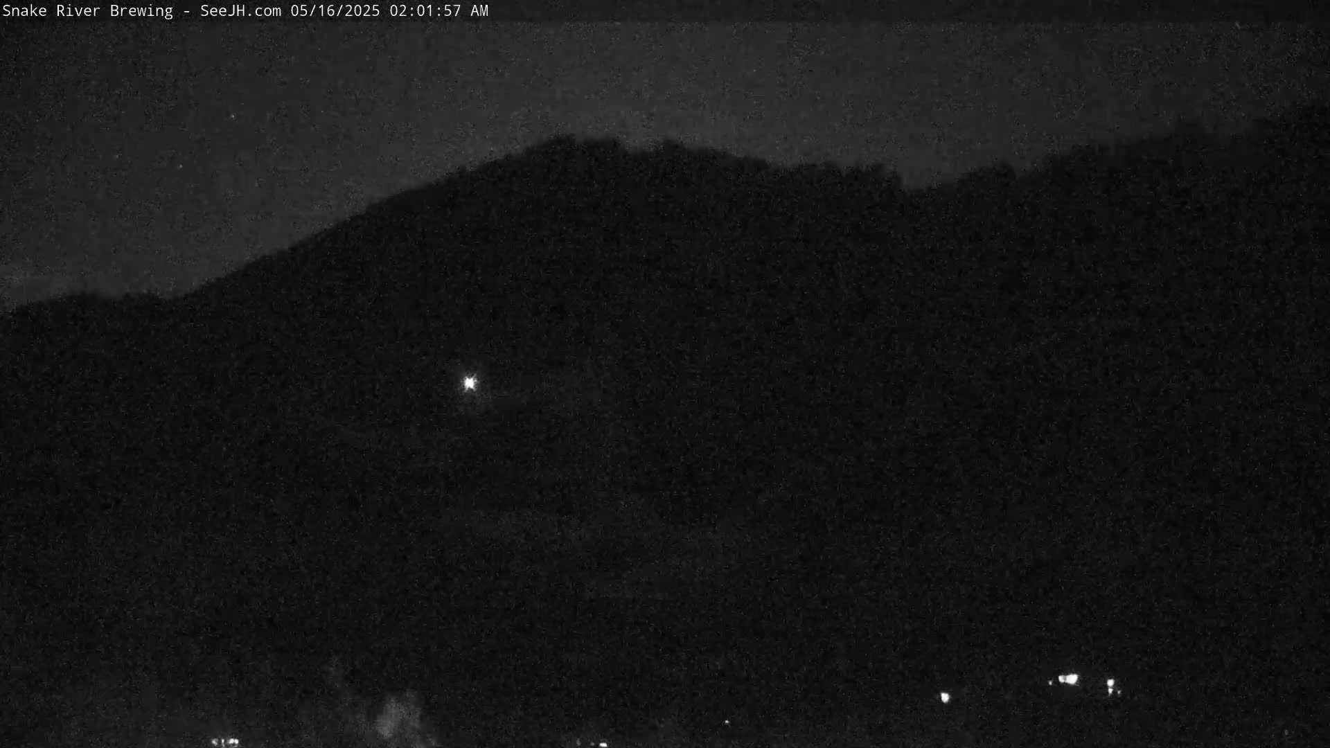 A nighttime view shows a dark, silhouetted hill under a clear, dark sky with a few faint lights visible in the distance.