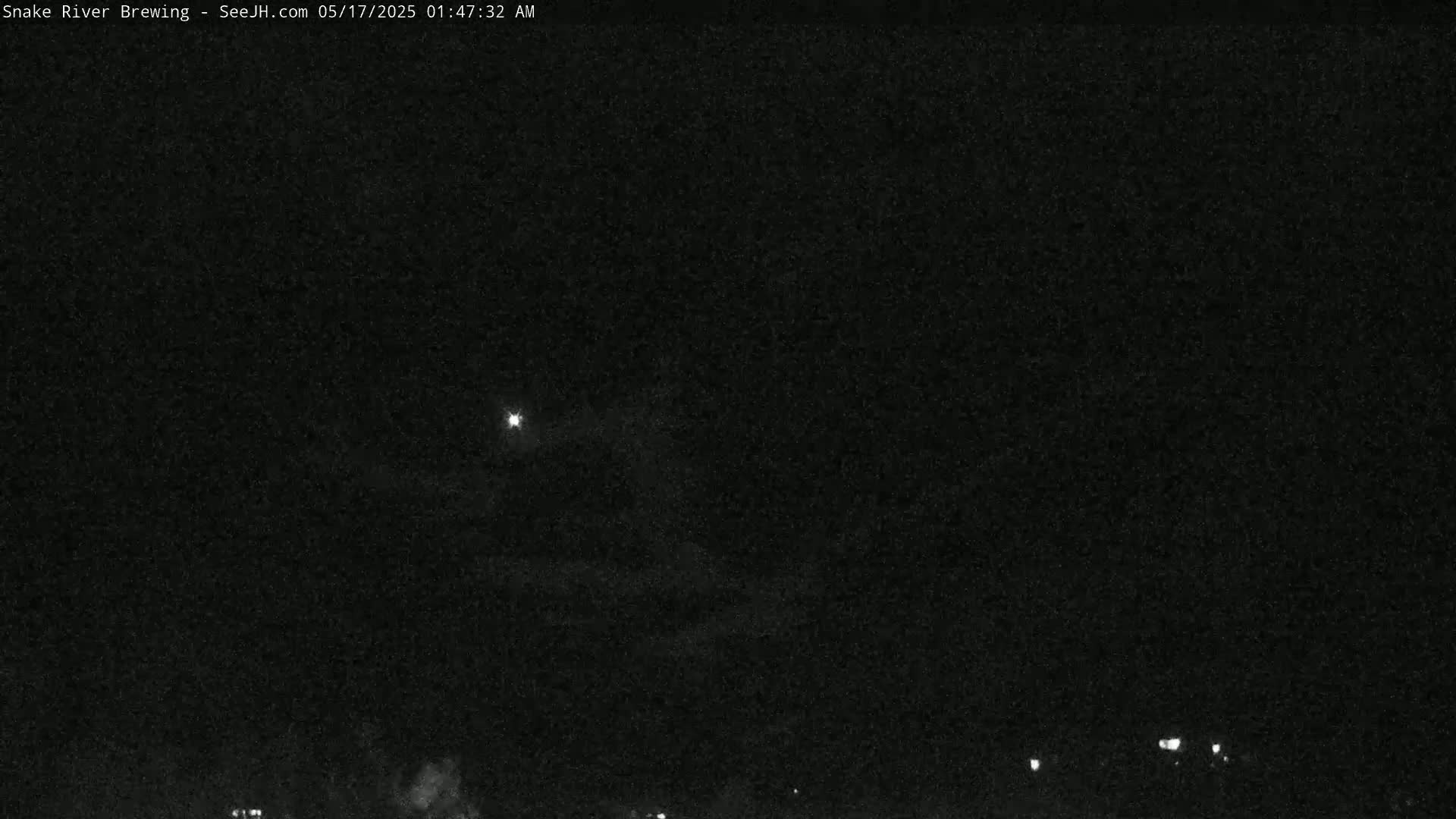 A nighttime, low-light outdoor image shows a bright light in the sky above a dark, flat horizon with a few small lights visible at the bottom.