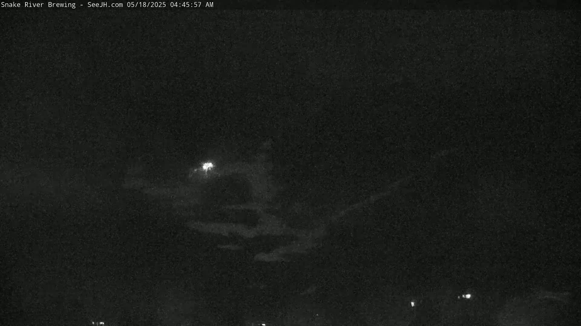 A nighttime, low-light view shows a mostly cloudy sky with a few faint lights visible on the ground.