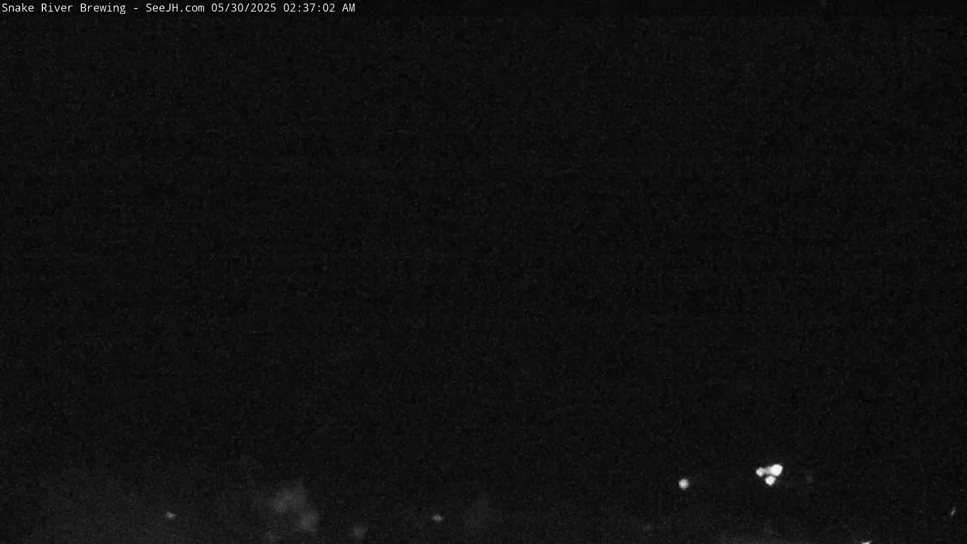 A nighttime, low-light image shows a dark, mostly featureless scene with a few faint lights visible in the lower portion.