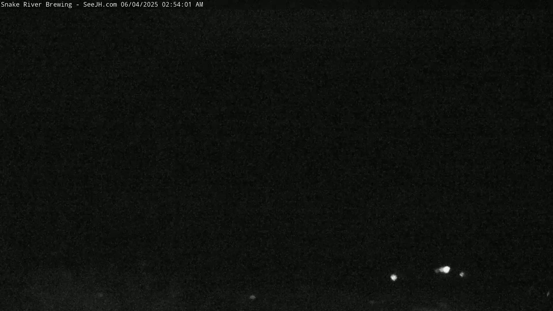 A nighttime, low-light outdoor image shows a dark, grainy scene with a few small, distant lights visible near the bottom.