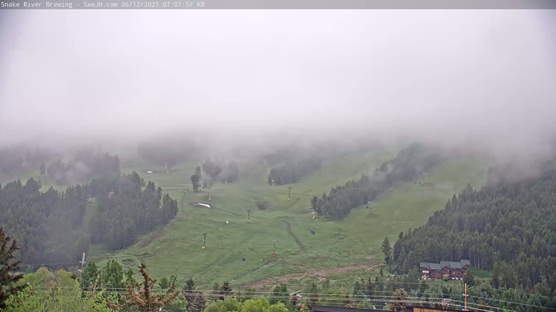 A foggy, green hillside with ski lifts and a cluster of buildings nestled among the trees in the lower right corner is visible.