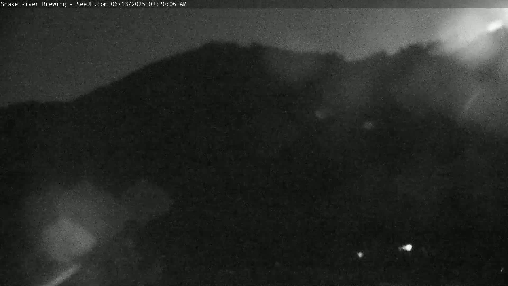 A dark, nighttime image shows a hill or mountain silhouetted against a dim sky.