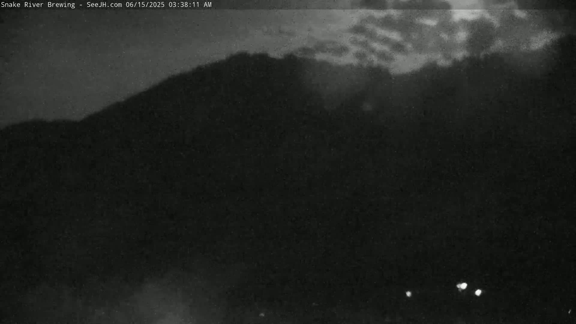 A dark, nighttime scene shows a silhouetted mountain under a cloudy sky.