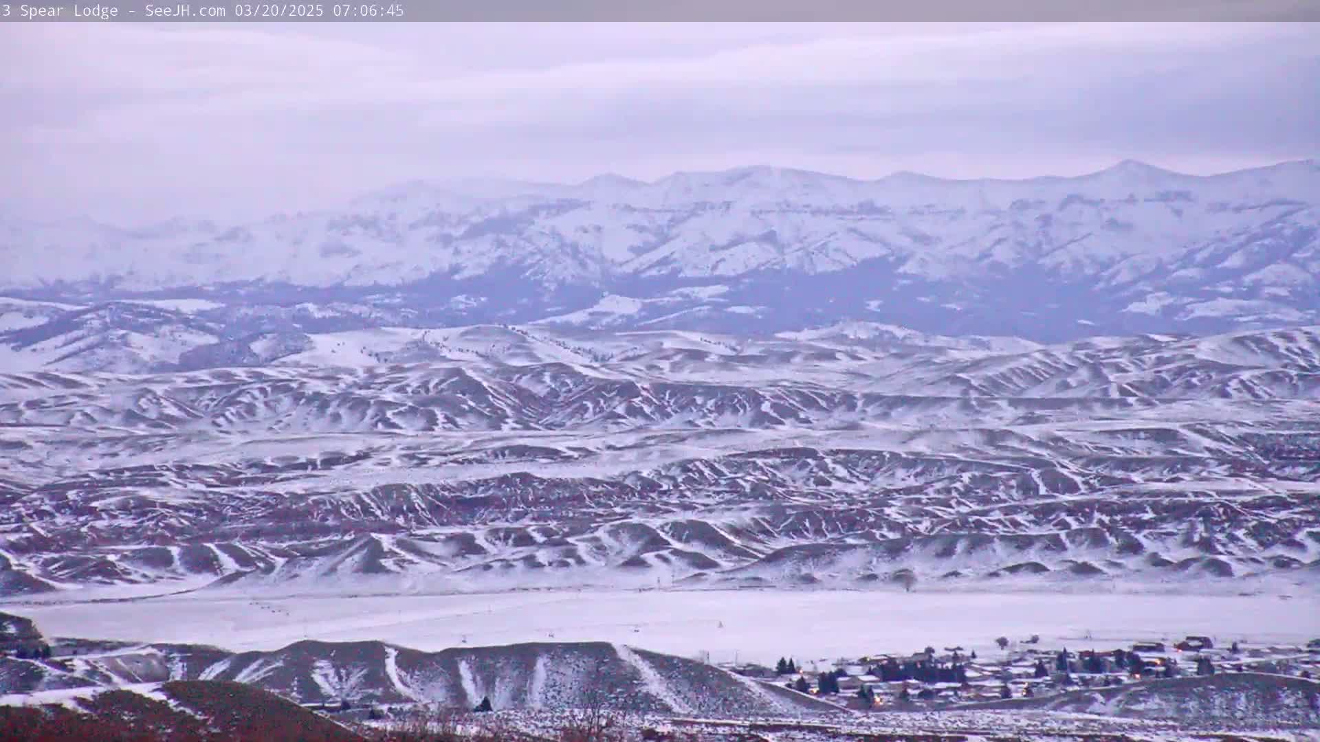 A snow-covered landscape of rolling hills and distant mountains under a cloudy sky.