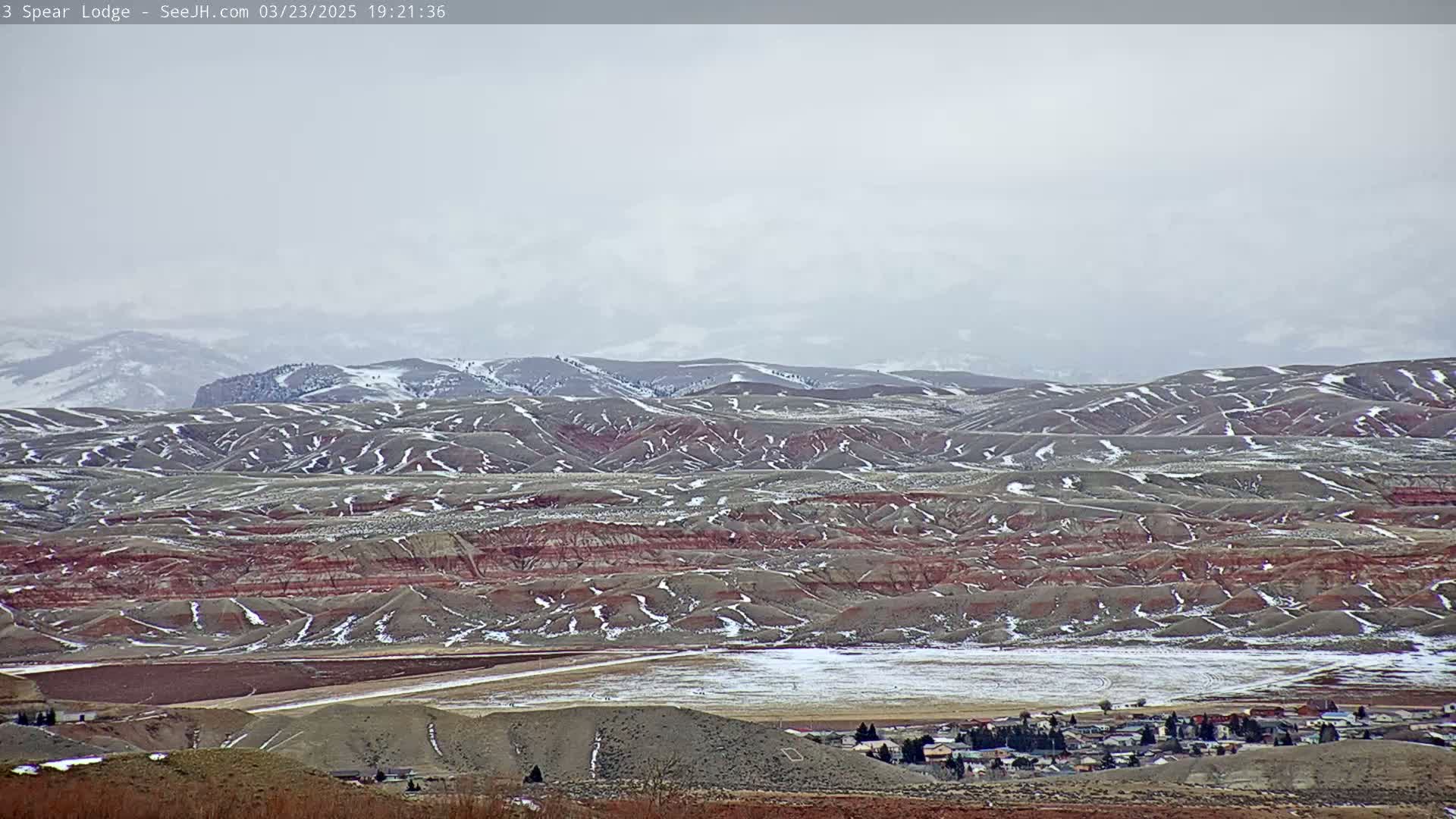 A snow-dusted landscape of rolling hills and a small town under an overcast sky.