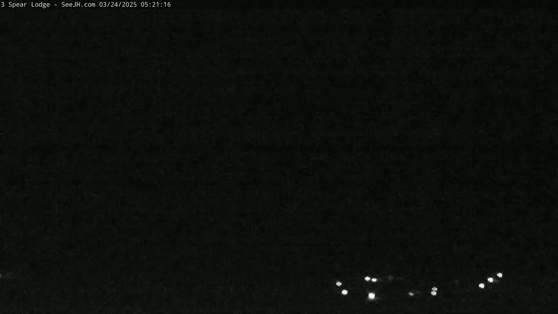 A nighttime, low-light image shows a few small, distant lights at the bottom of the frame against a completely dark background.